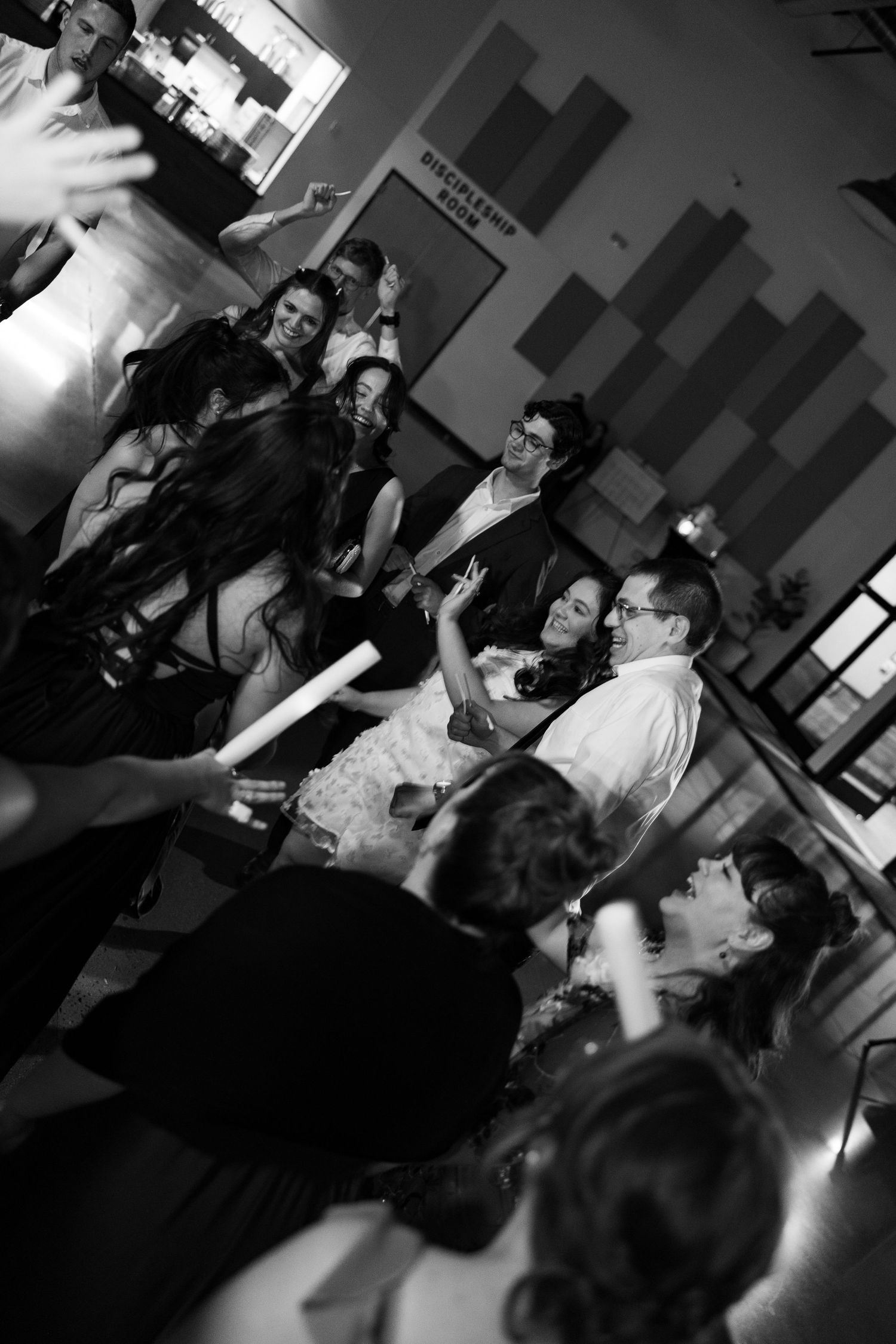 Black and white photo of guests dancing and celebrating at a lively wedding reception party.