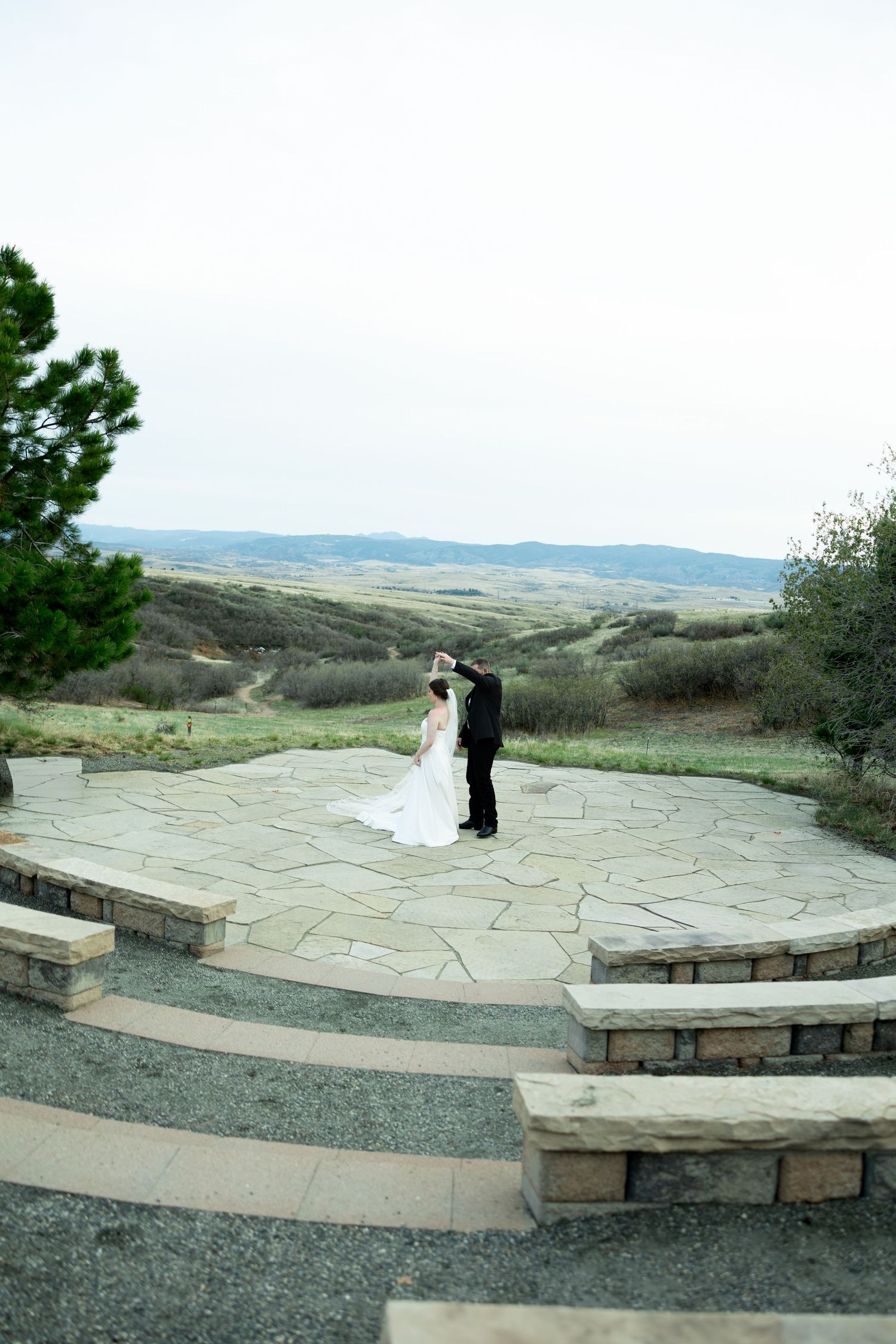 Bride and groom share a romantic moment on a stone patio overlooking scenic rolling hills at an outdoor wedding venue.