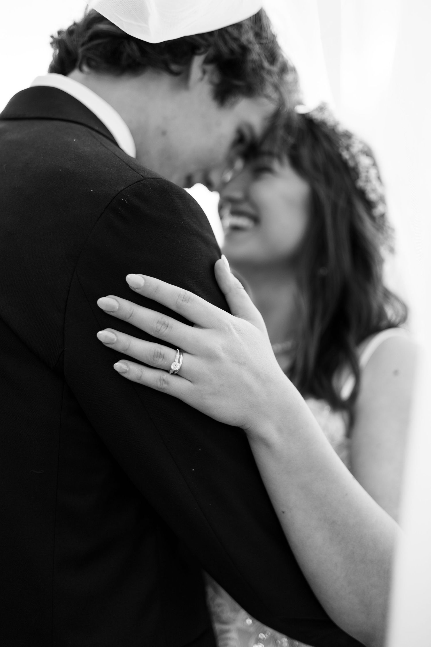 Black and white close-up of newlyweds embracing shows engagement ring detail.