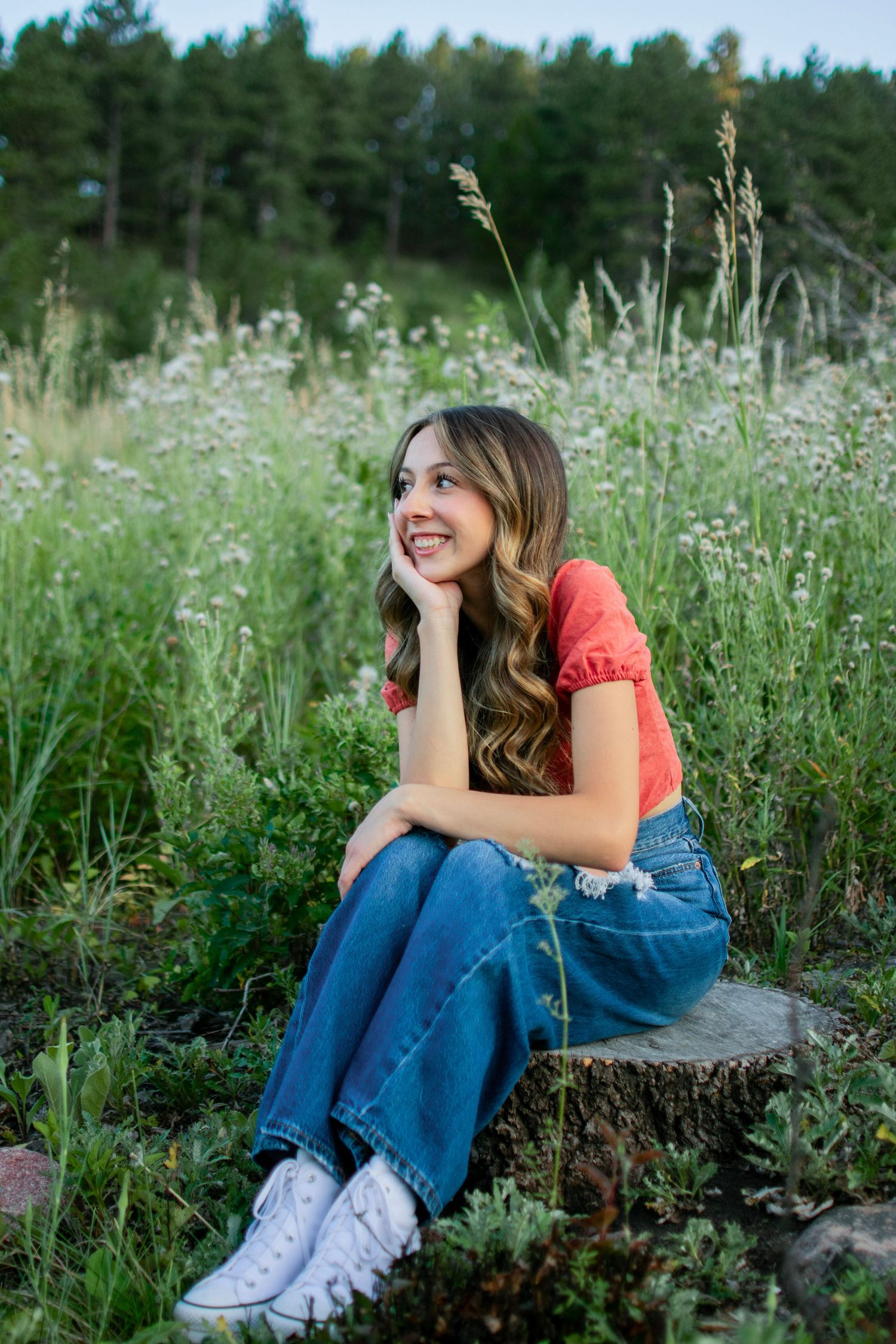 A person in a coral top and jeans sits casually in a wildflower meadow on a summer evening.