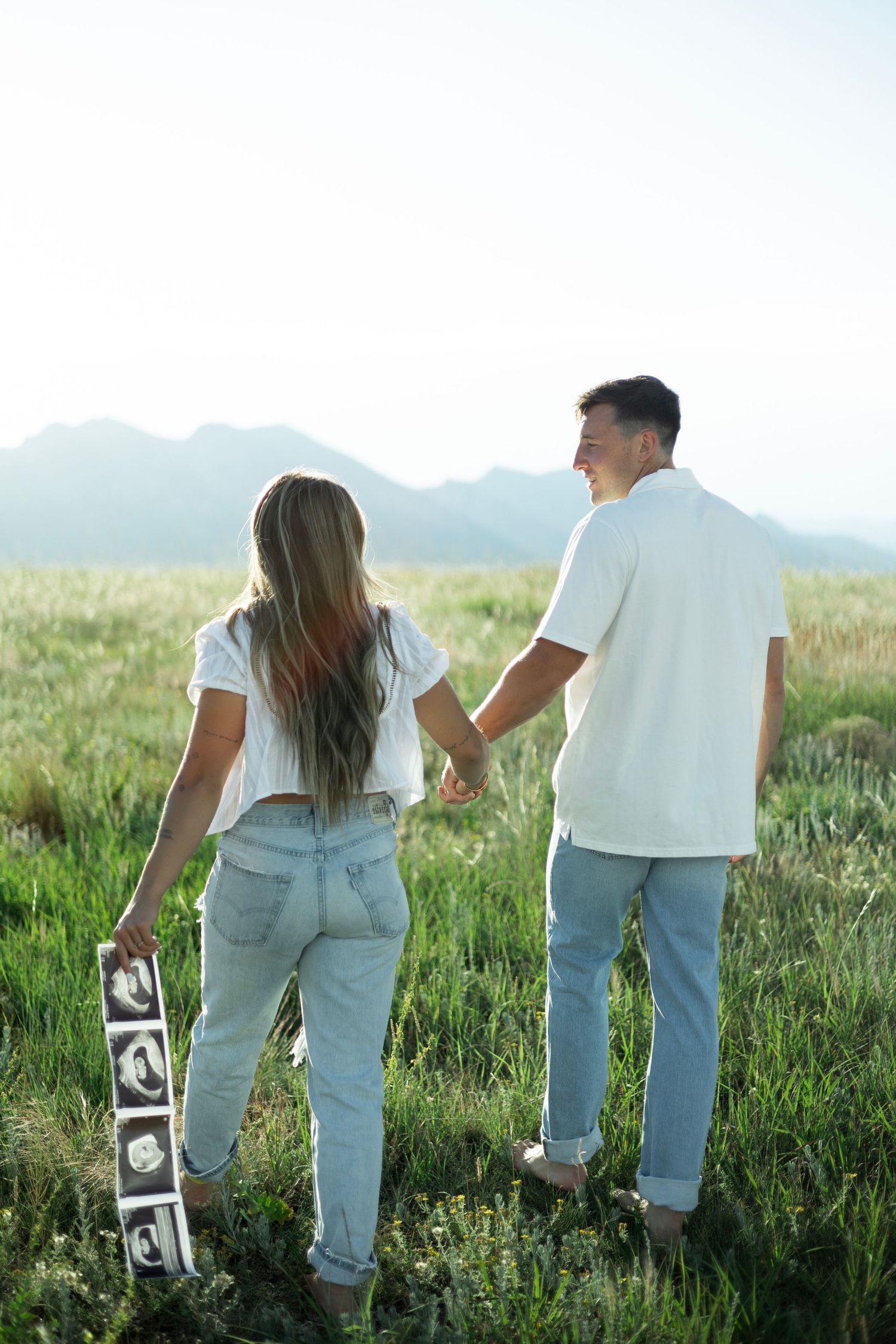 Couple holding hands walking in meadow with mountain view while holding ABC blocks on sunny day.