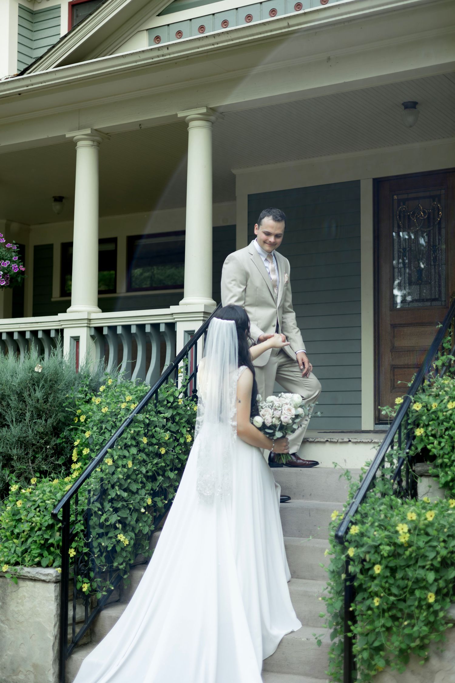 A couple shares a romantic moment on a front porch with white columns surrounded by lush greenery.