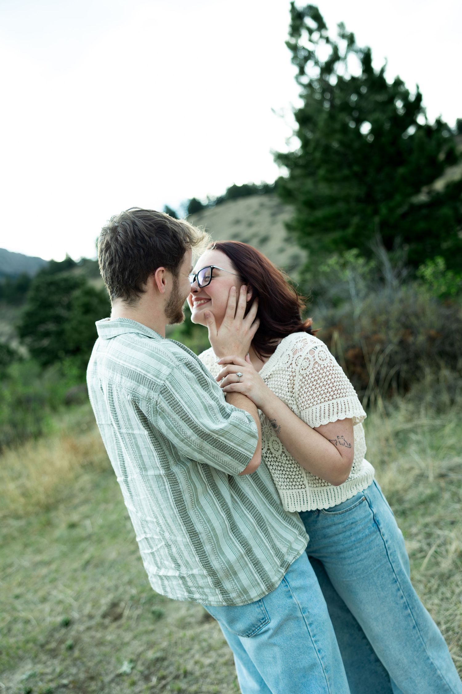 Couple embracing and laughing together outdoors in a green hillside setting, woman wearing sunglasses and crochet top.