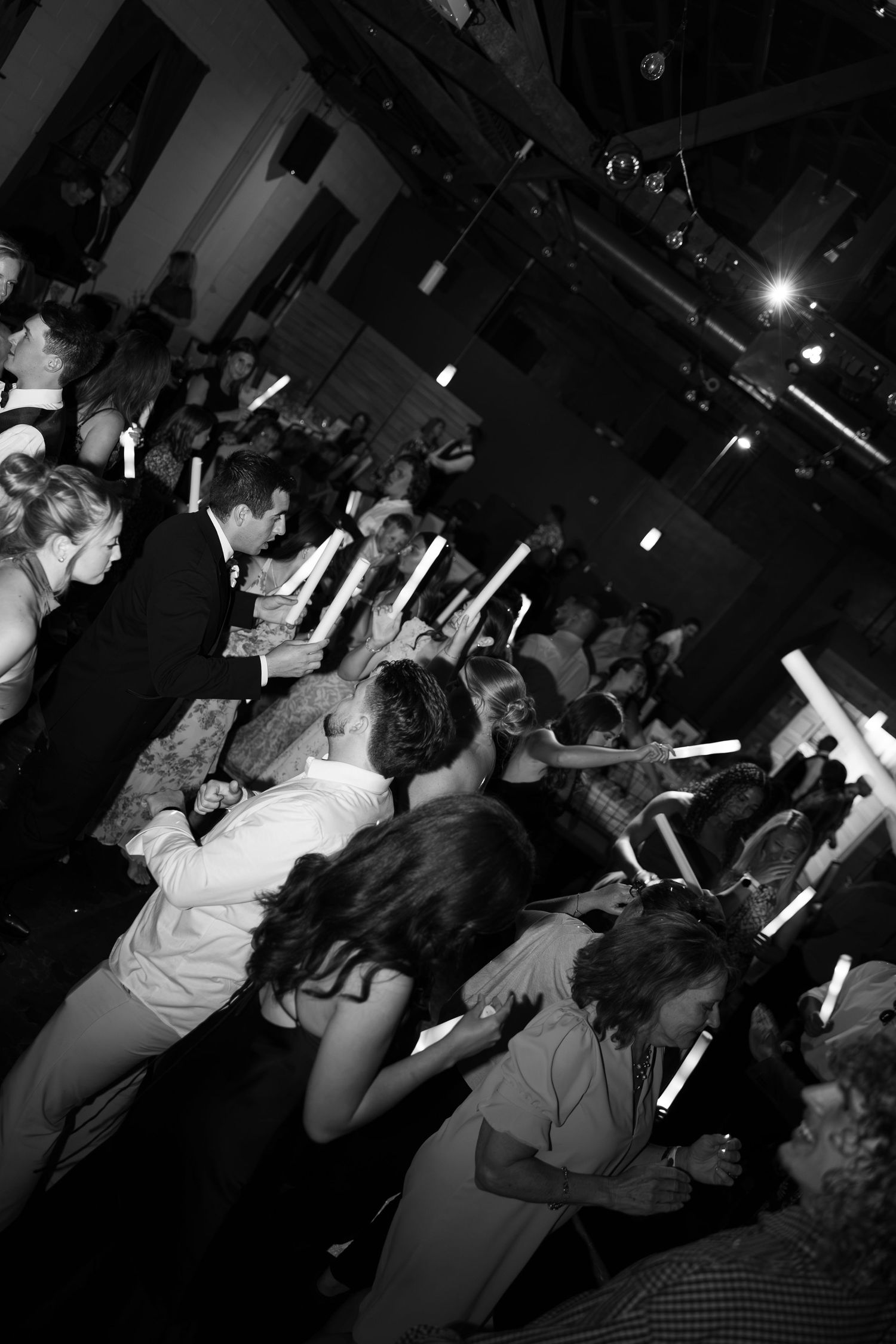 Black and white photo of wedding reception guests dancing and holding glowing candles in a dimly lit venue.