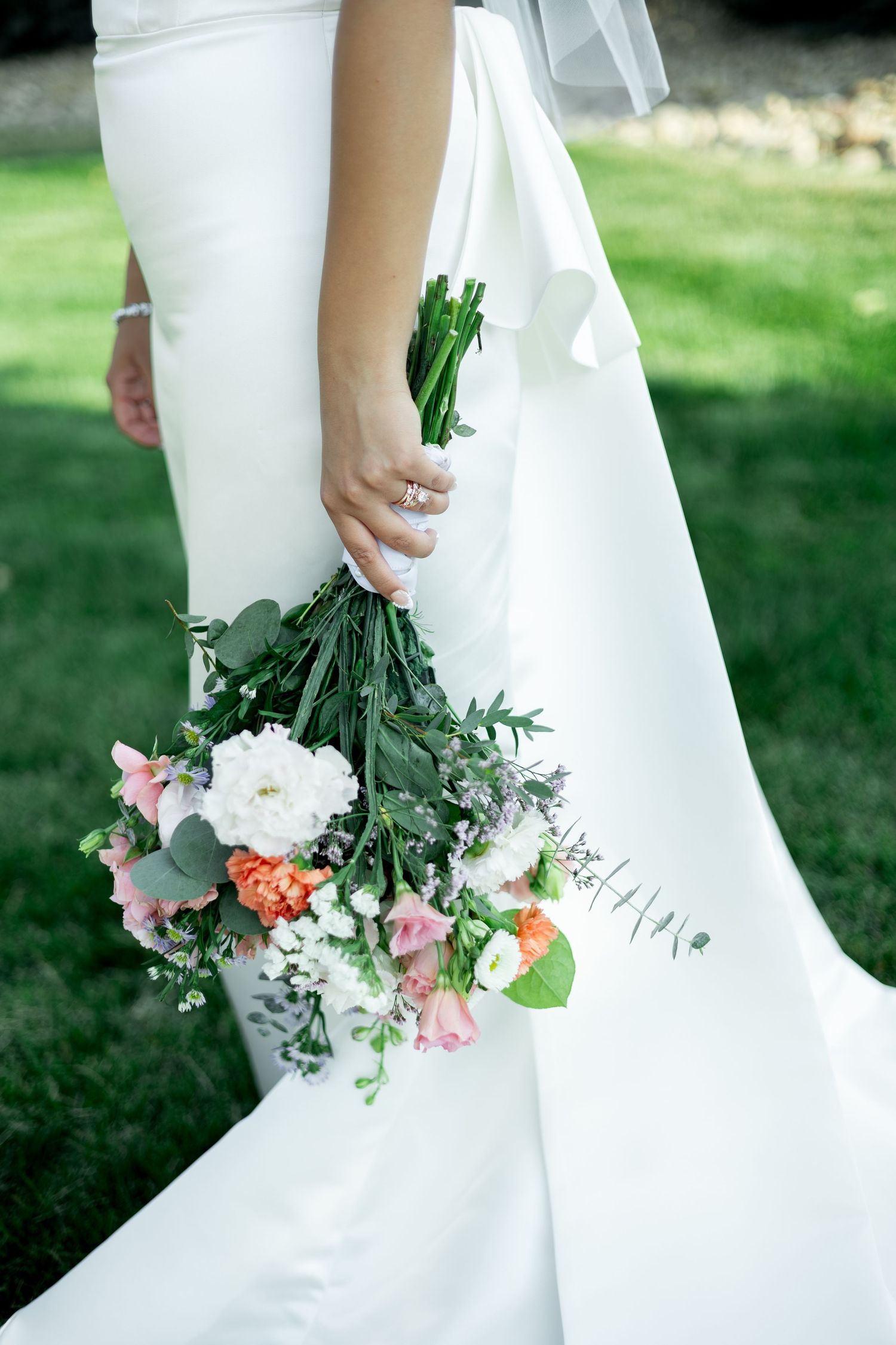 Bride in white gown holding a loose cascading bouquet of pink, white, and orange flowers with eucalyptus greenery.