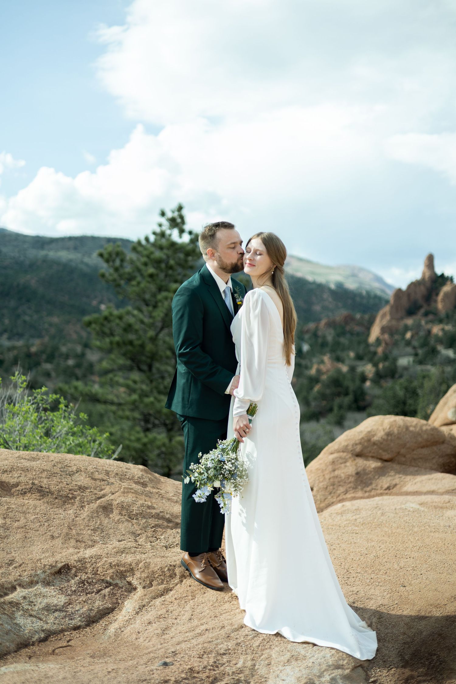 Bride and groom pose on red rocks with mountain backdrop at Garden of the Gods wedding in Colorado.