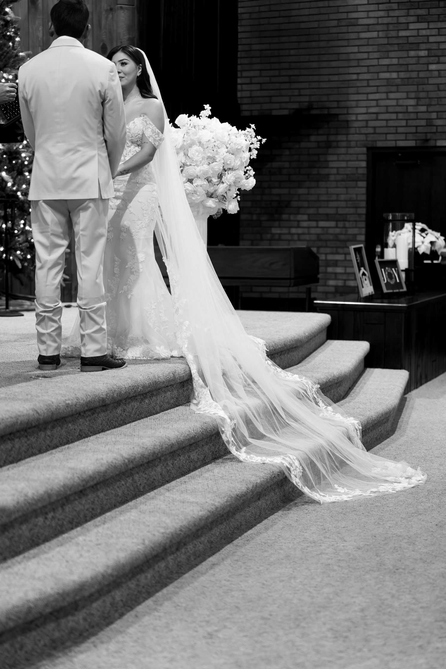 A bride in a flowing white dress poses gracefully on stone steps in black and white.