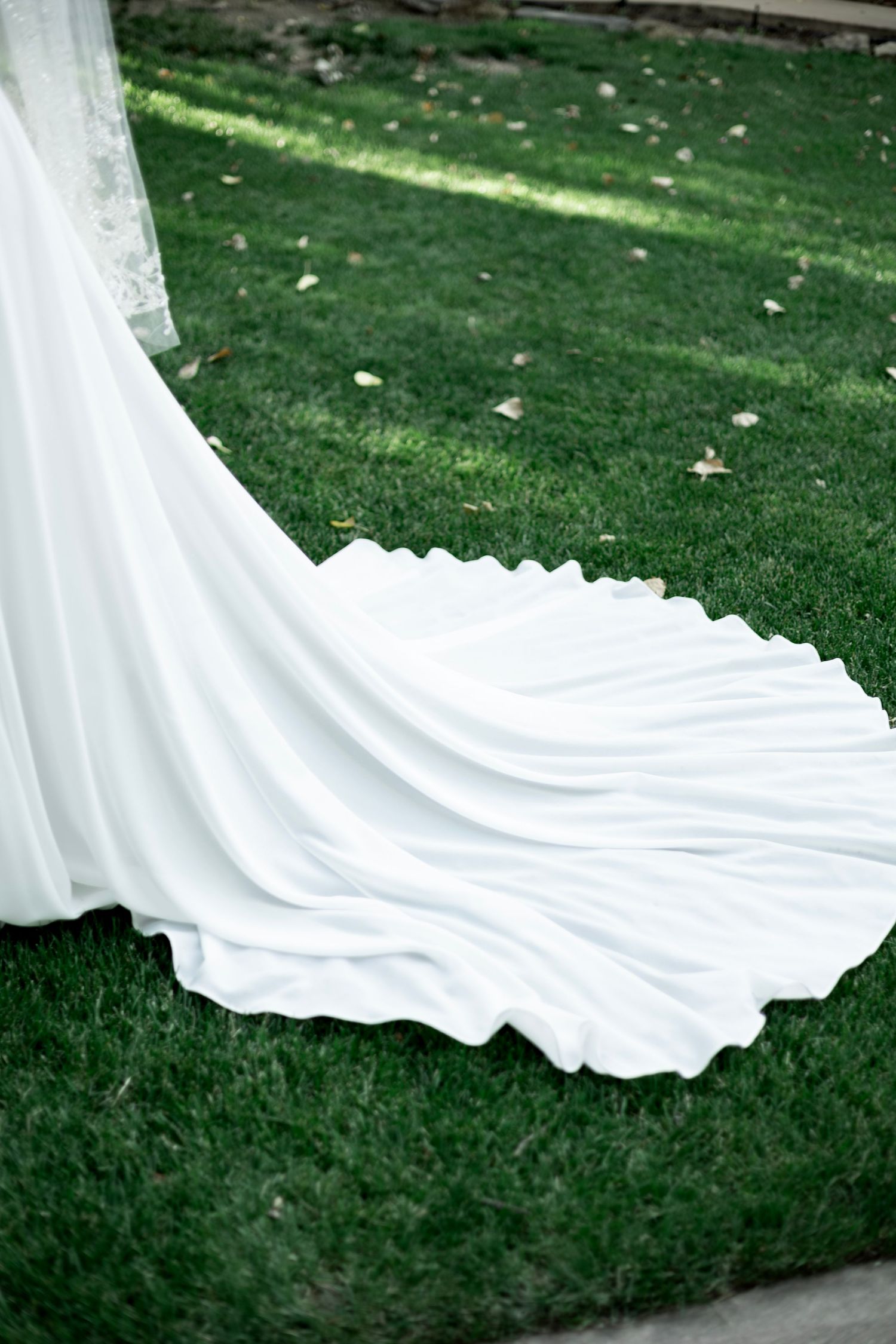 Elegant white wedding dress train flowing over green grass with scattered autumn leaves.