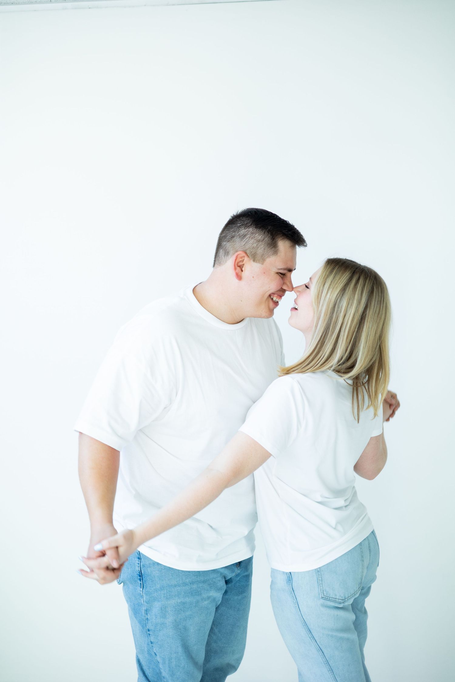 A couple in matching white t-shirts and blue jeans share an intimate moment against a light background.