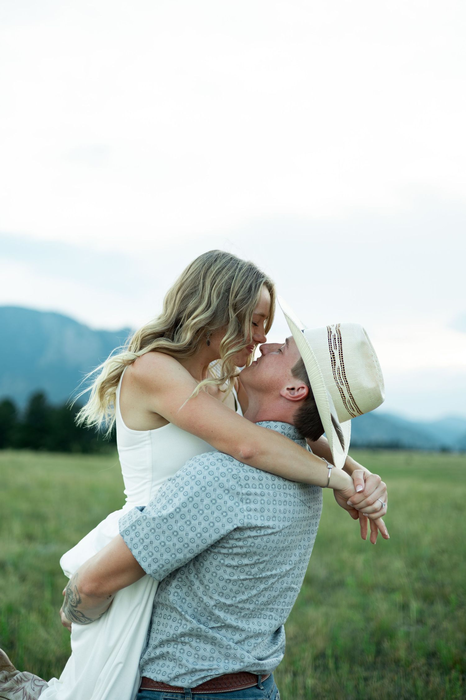 A couple embraces romantically in a series of tender poses against a scenic mountain meadow background.
