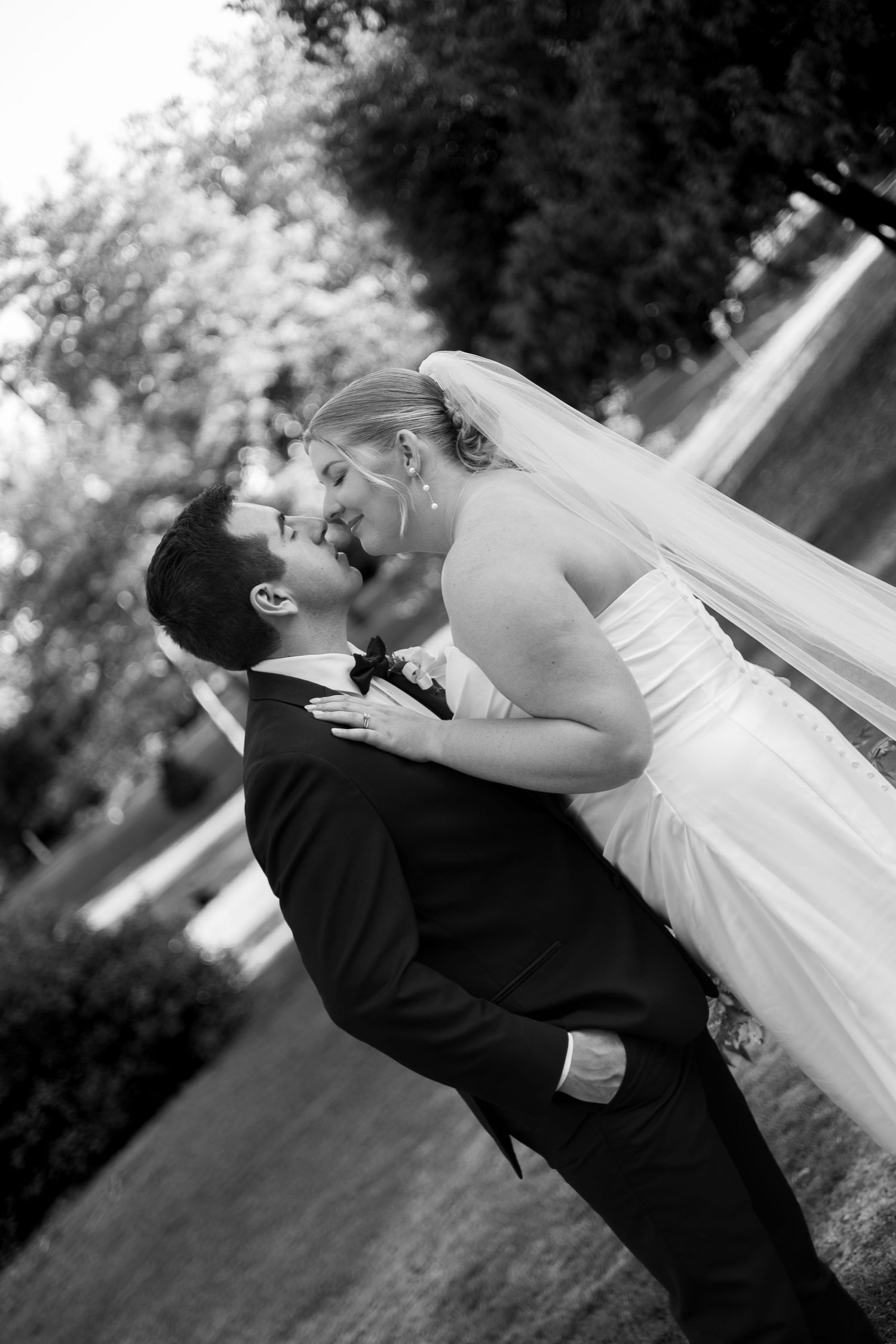 Black and white photo of a groom lifting his bride in a romantic outdoor wedding portrait.