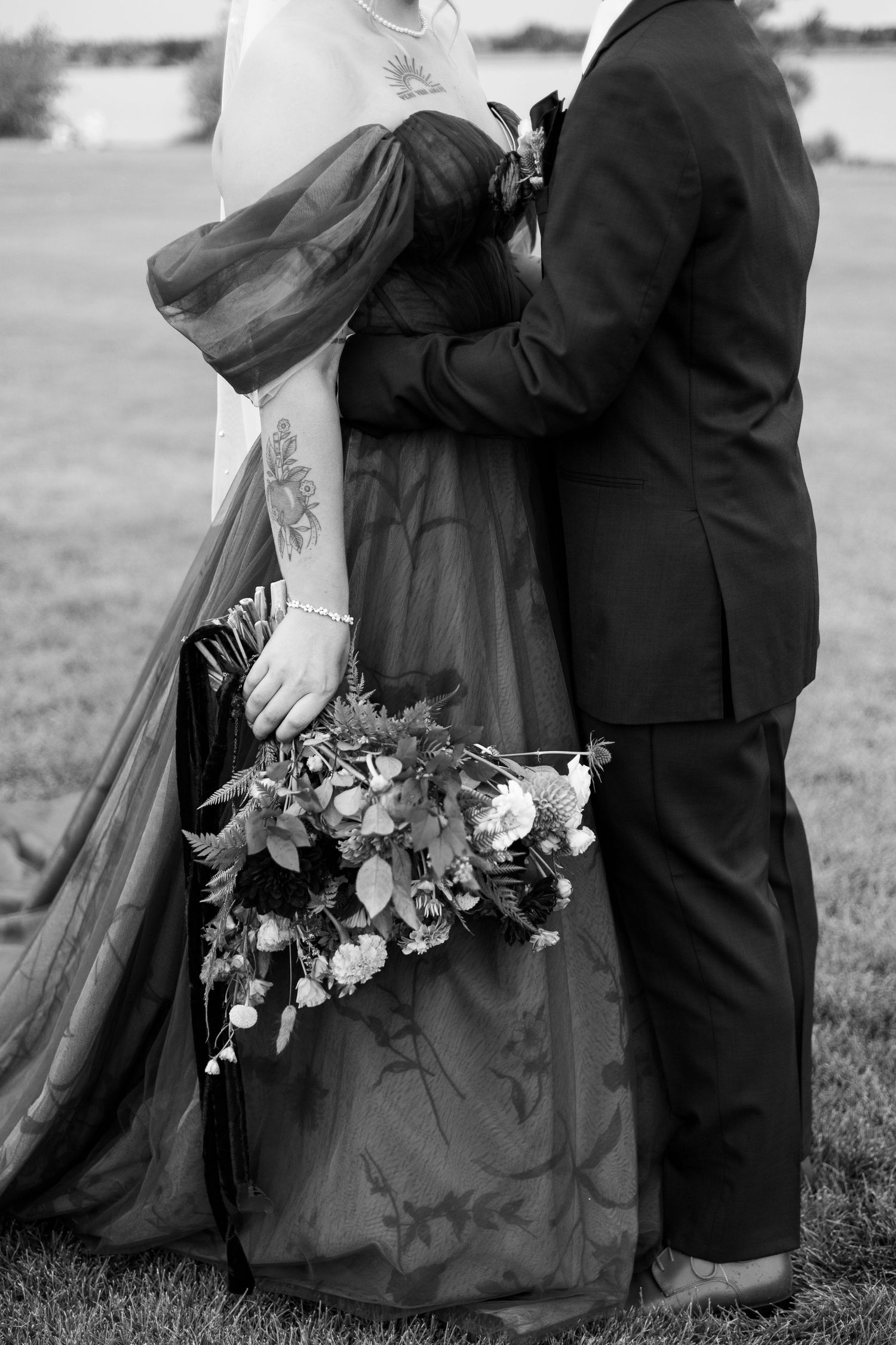 Black and white wedding photo showing a couple embracing with a bouquet of flowers against a blurred outdoor background.