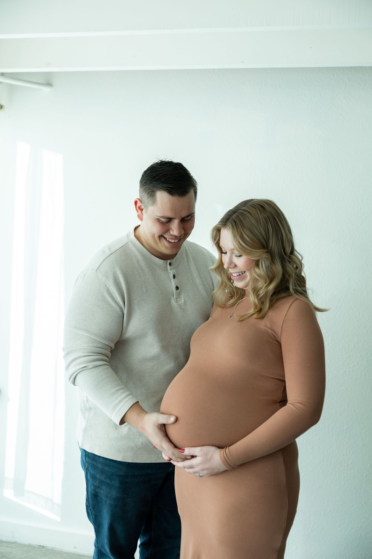 A couple shares an intimate moment while standing together in a bright, minimalist room with white walls.