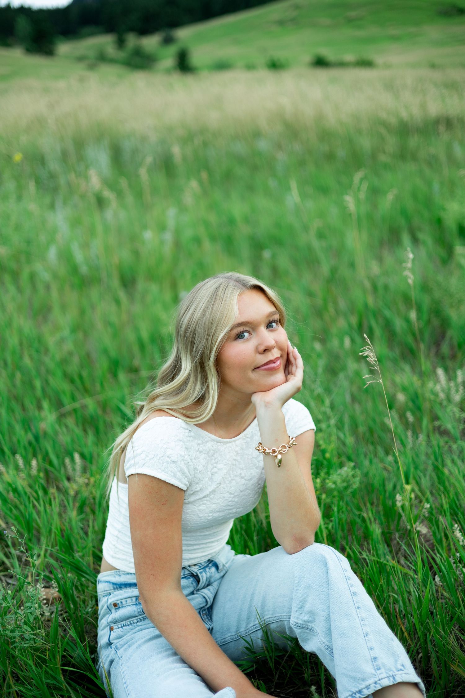 A person in a white top and light jeans sits relaxed in a lush green meadow on a summer day.