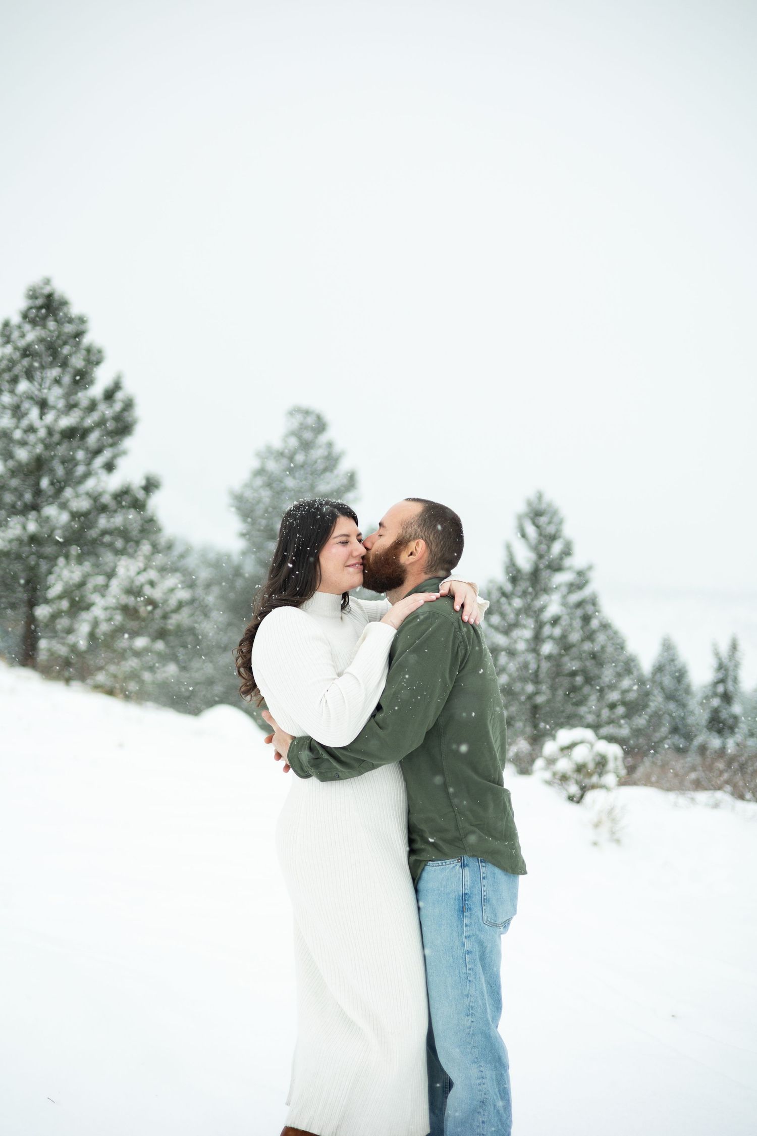 A couple shares an intimate moment in a snowy winter forest setting.