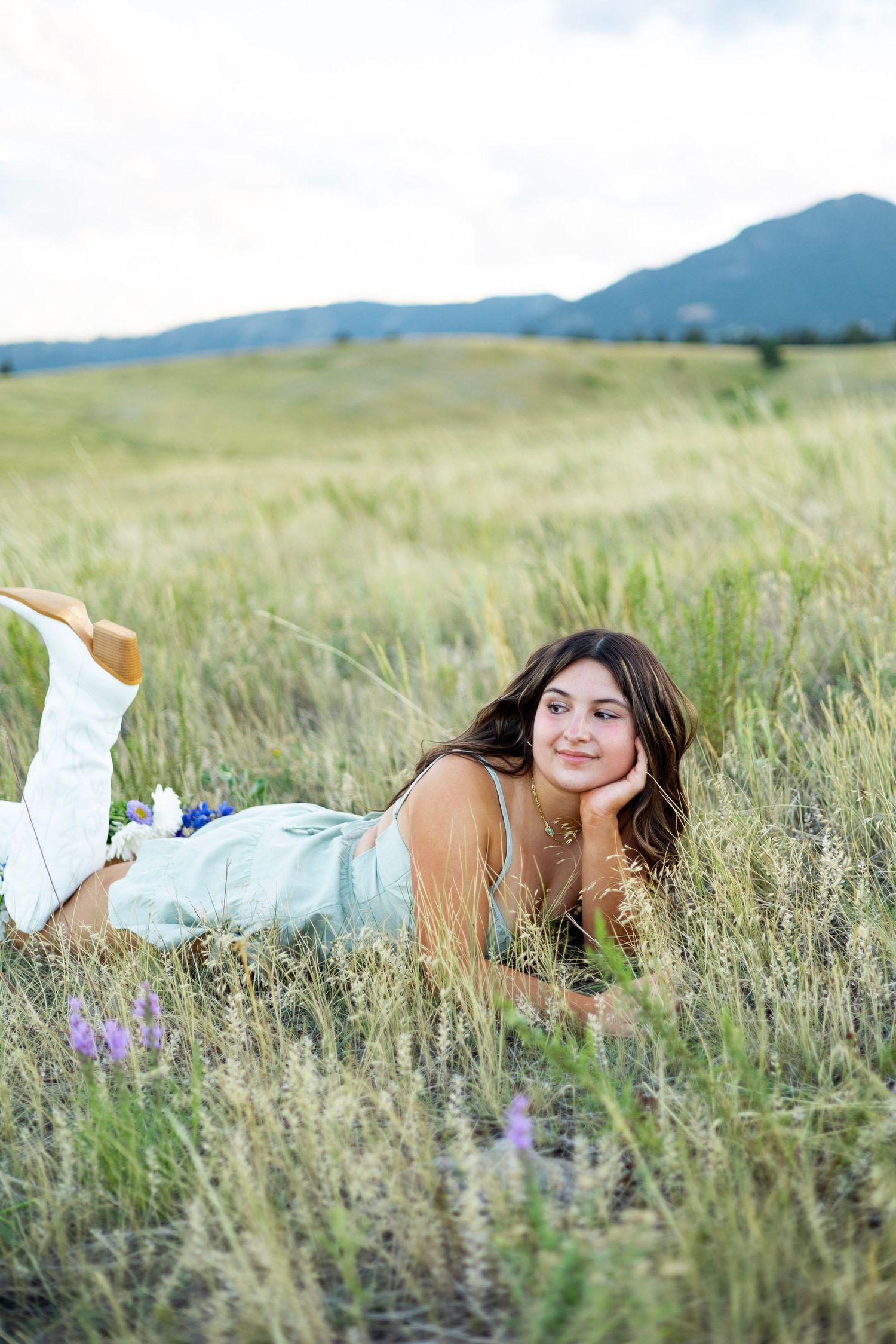 Person in light blue dress lying in mountain meadow with wildflowers.