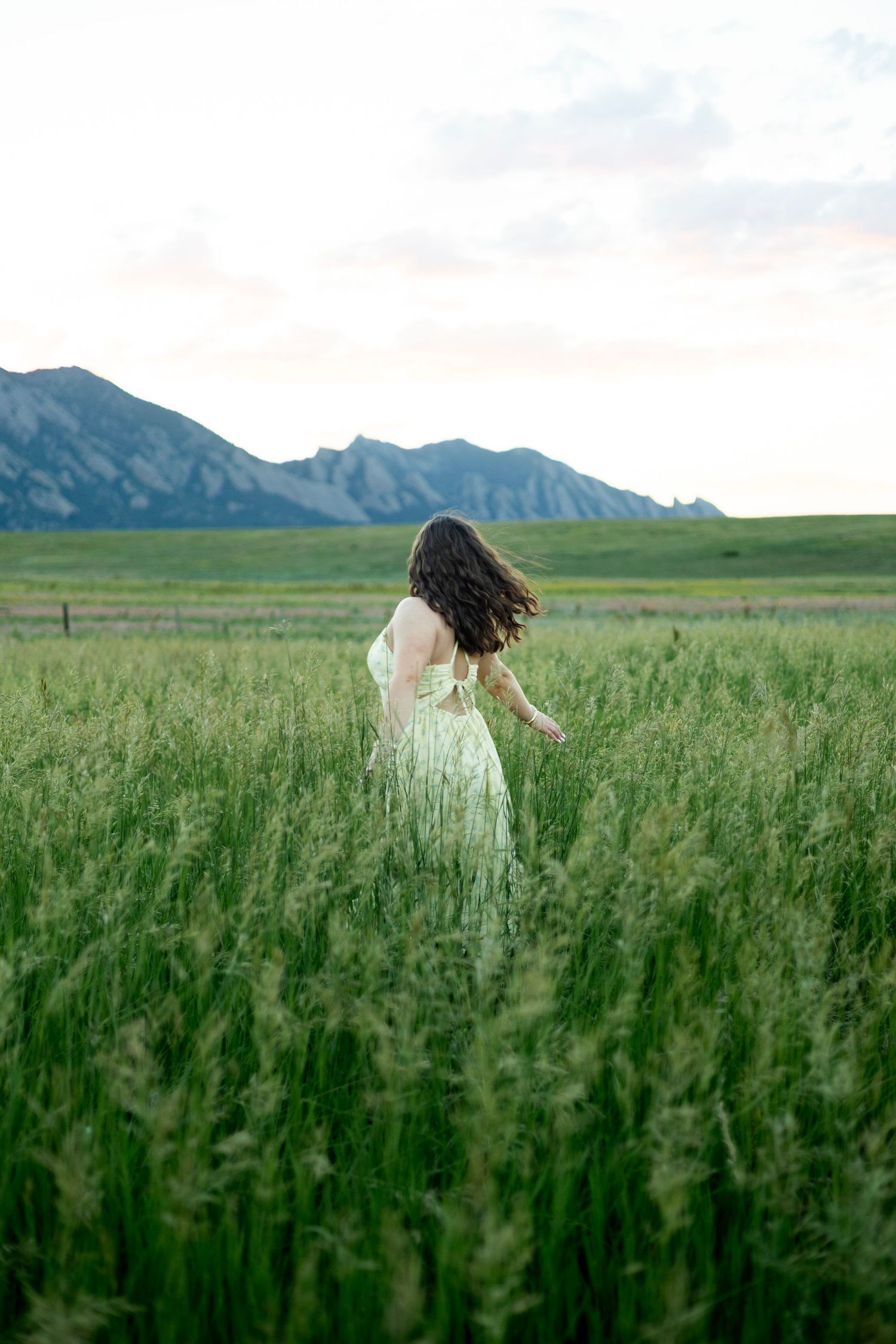 Woman in green dress walking through tall grass field with Rocky Mountain Flatirons in background.