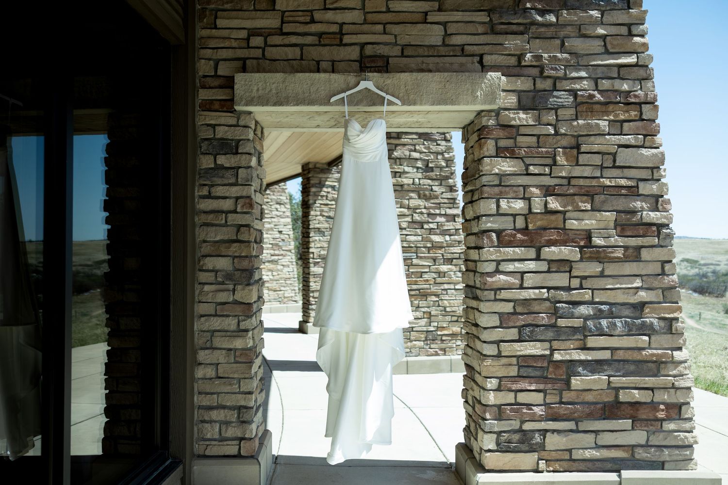 White wedding dress hanging between stone pillars with scenic landscape views in the background.