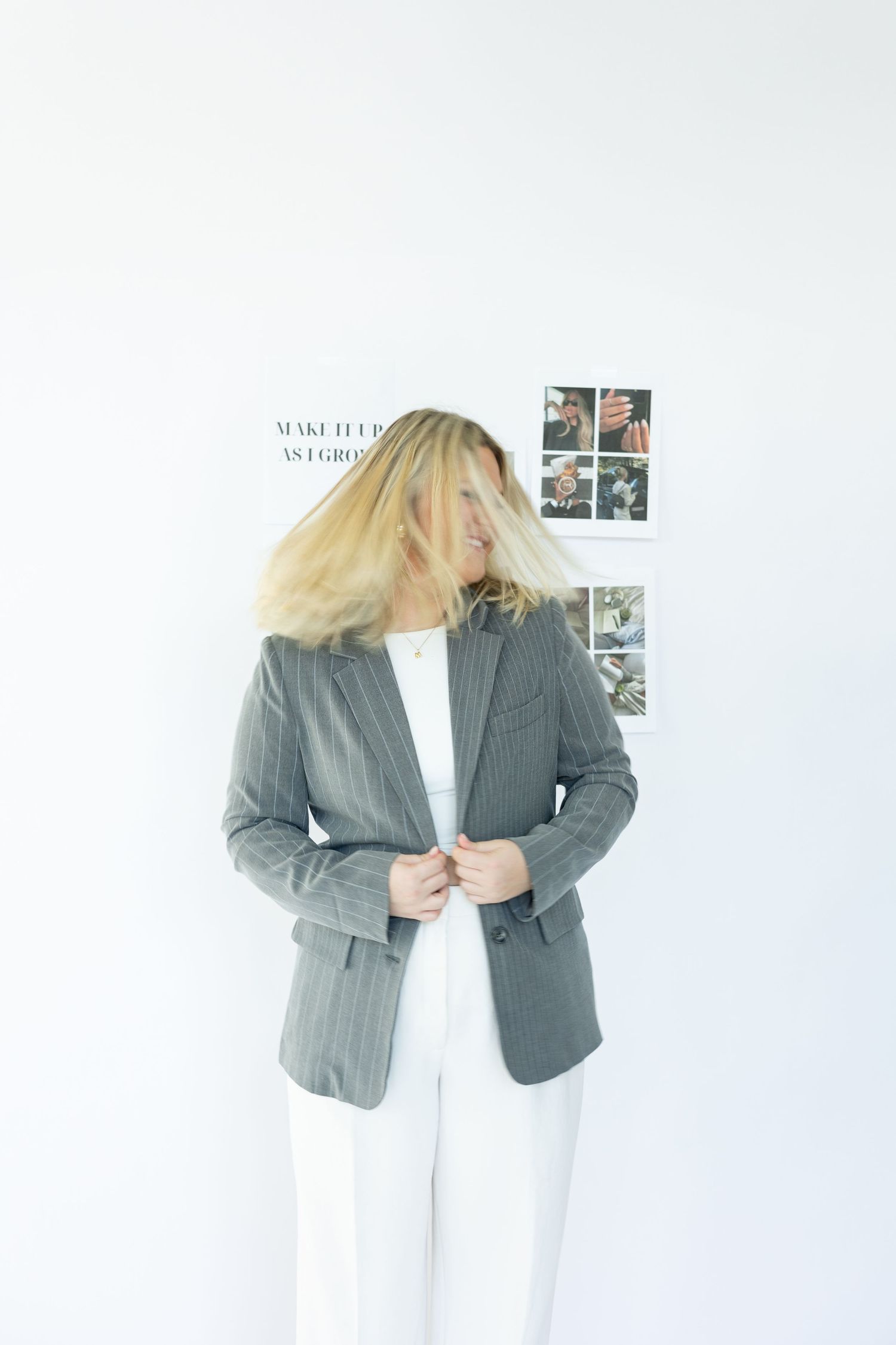 Person in gray blazer and white pants with dynamic hair movement pose.