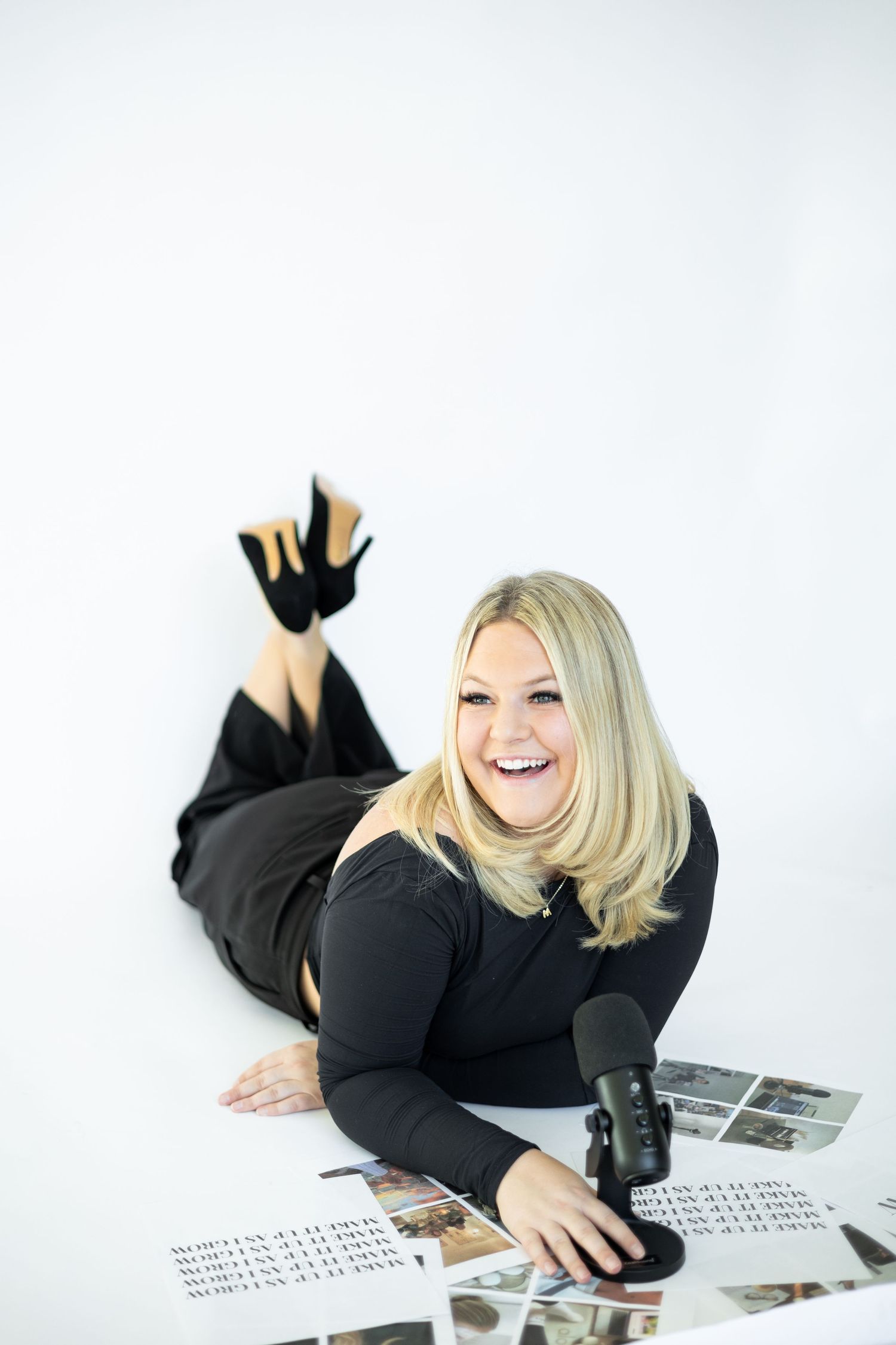Person lying on floor surrounded by photos and microphone with playful expression.