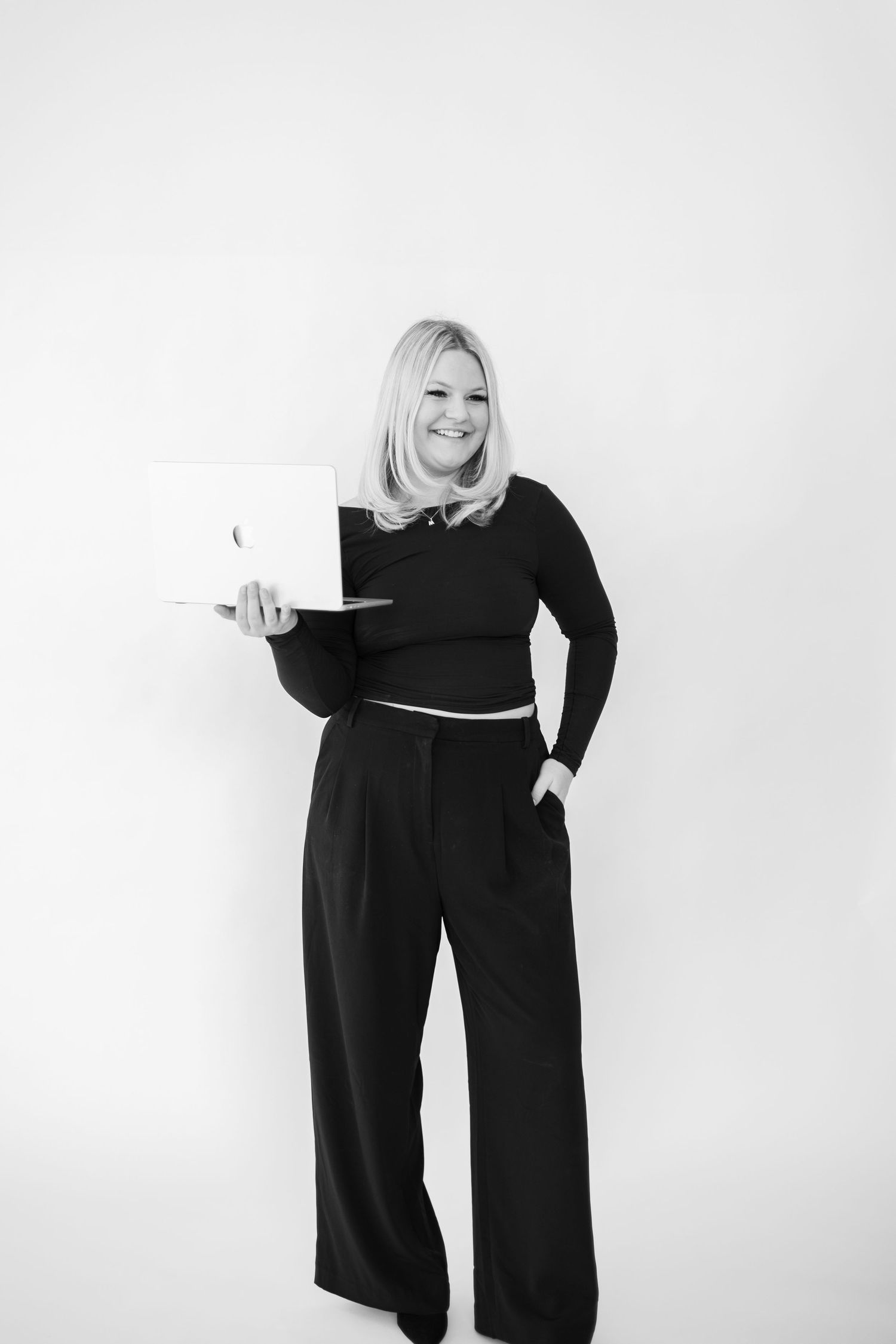Professional studio portrait of person in black outfit holding laptop against white background.