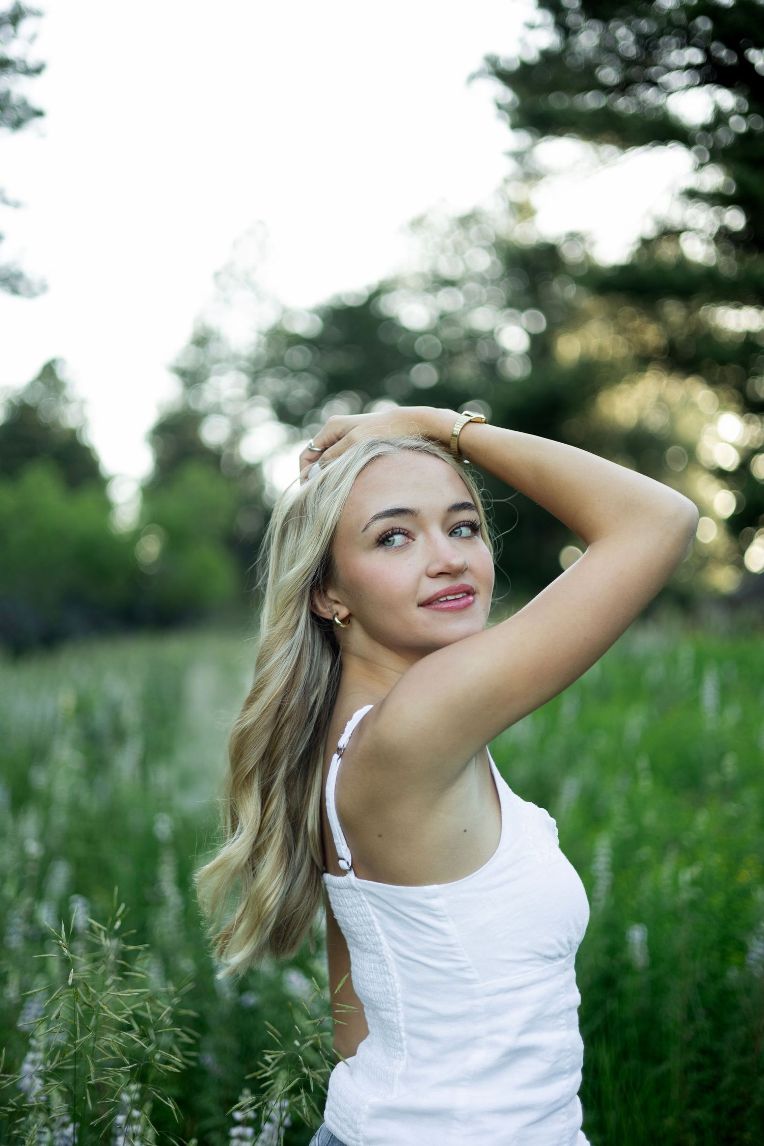Natural outdoor portrait with soft bokeh among tall grasses and evergreen trees at sunset.