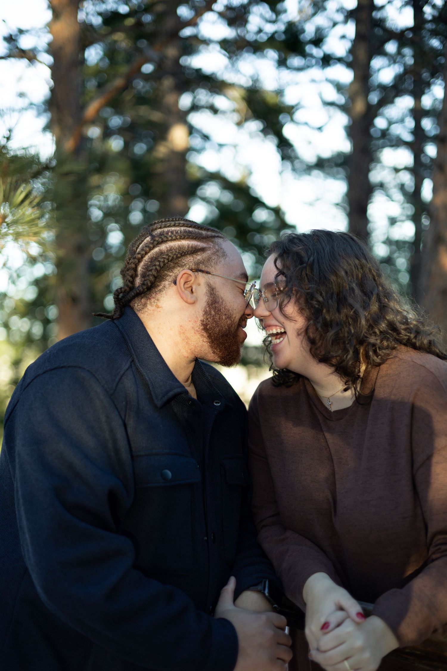 Intimate close-up moment between two people with pine trees in the background.