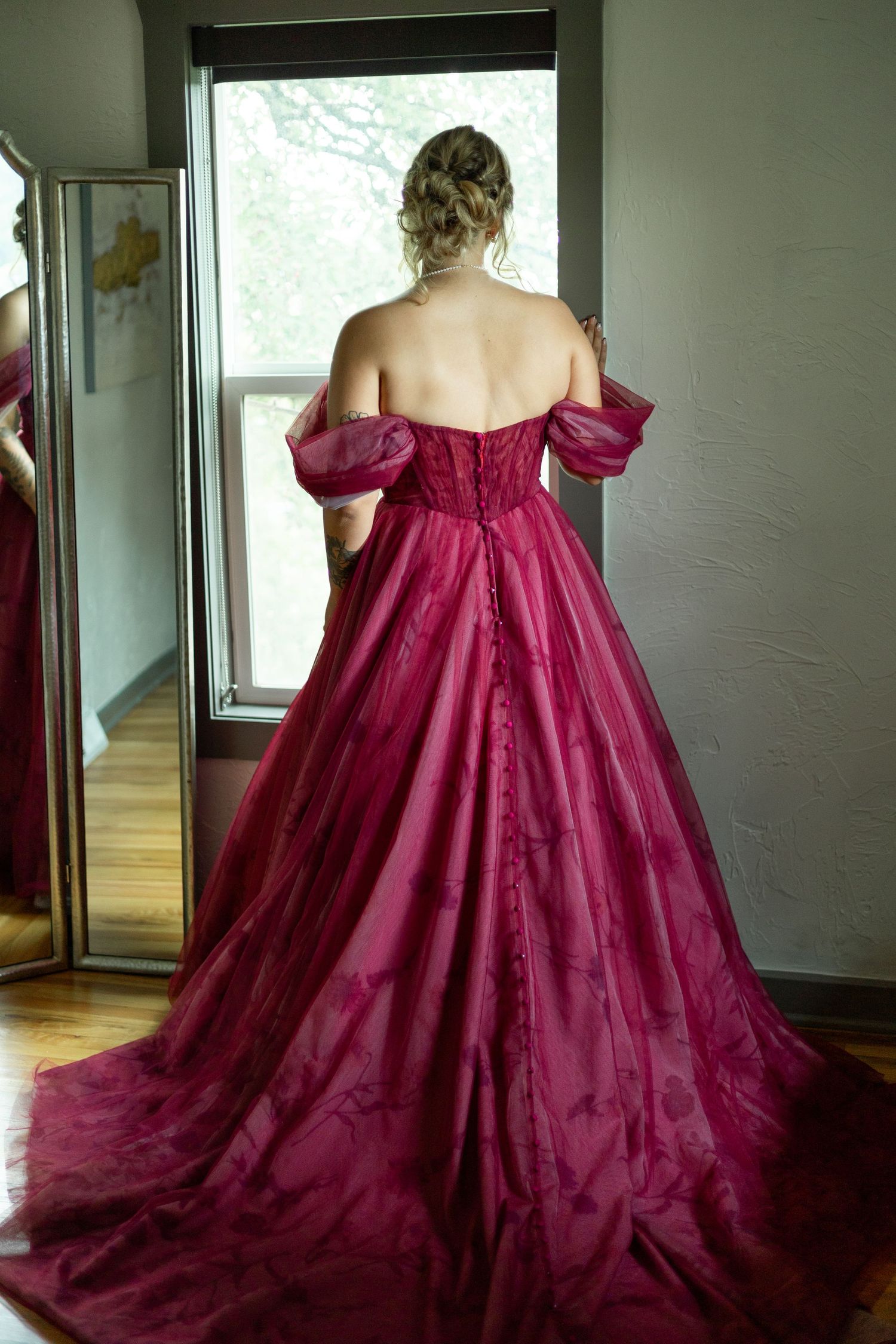 Back view of a burgundy ballgown with off-shoulder details and flowing train.