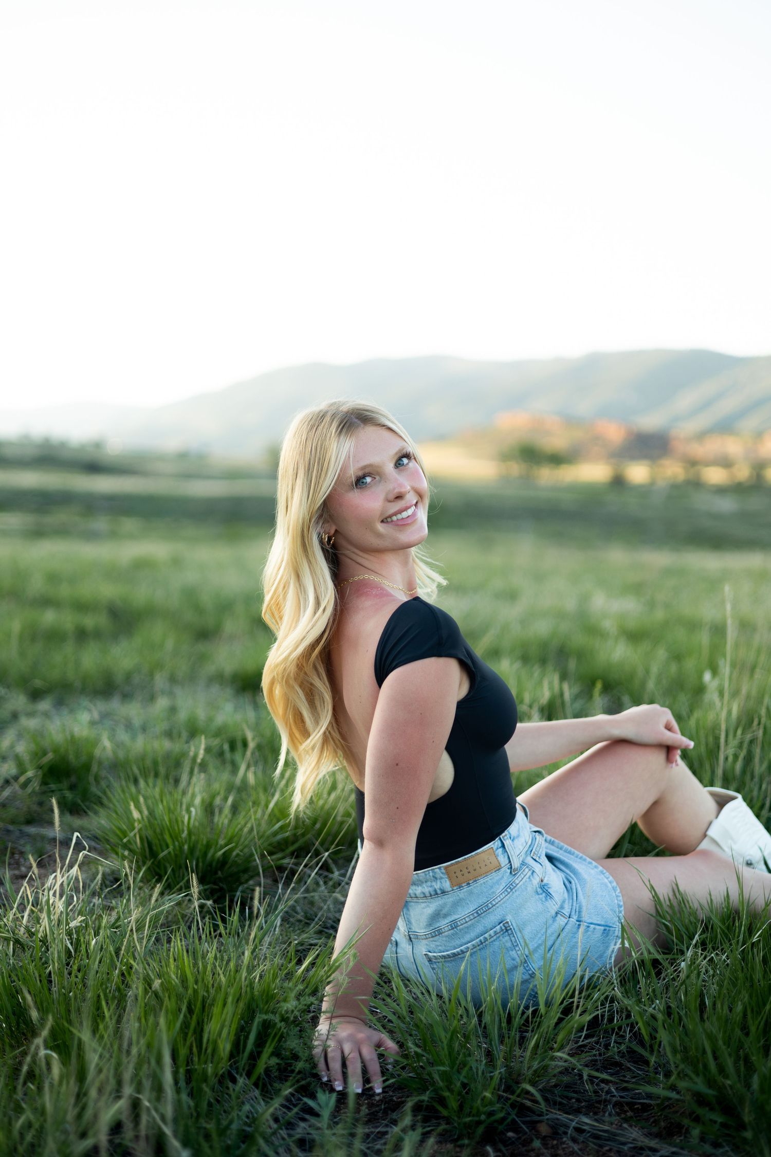 A relaxed summer portrait in a grassy field with mountains in the background at golden hour.