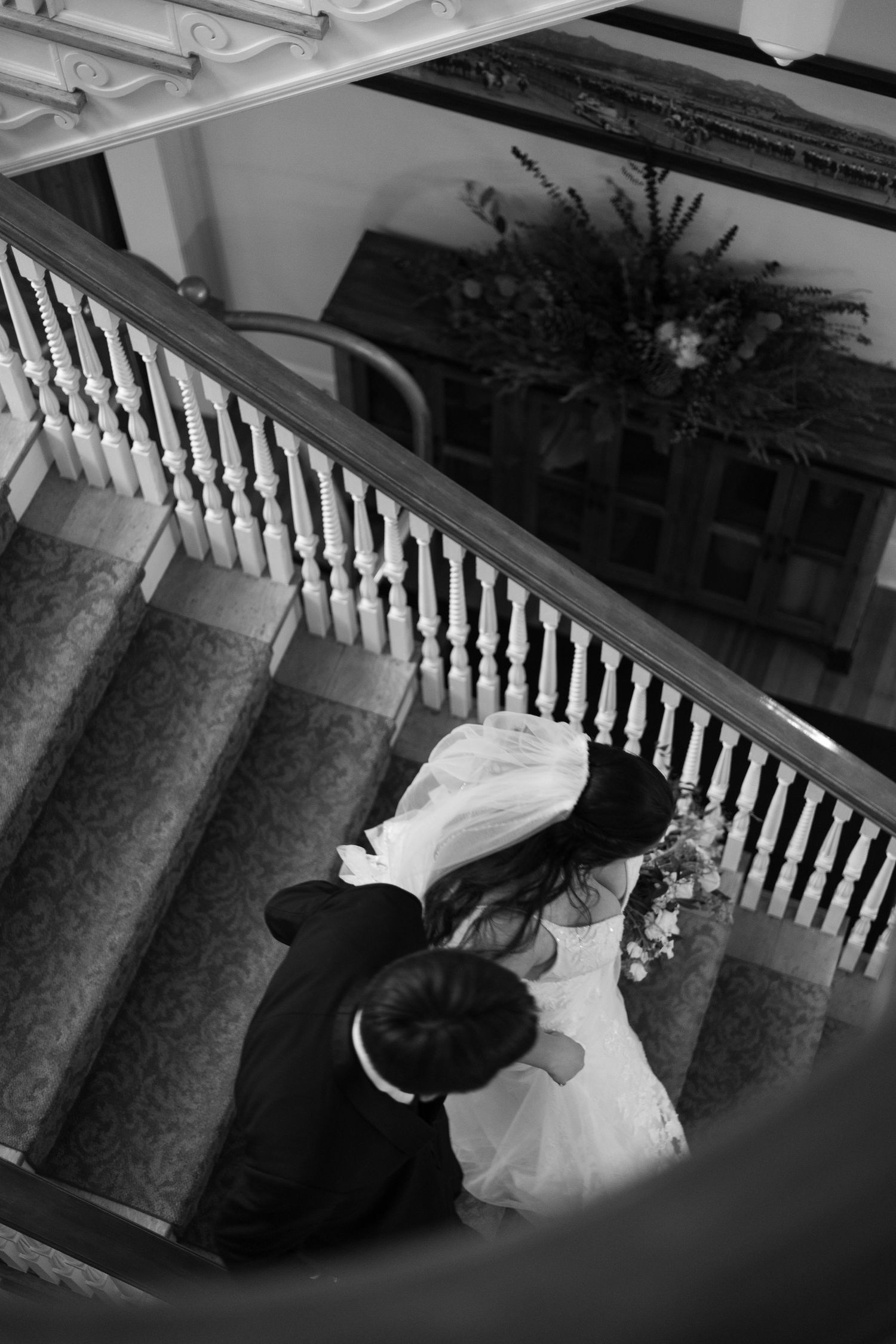 Black and white aerial view of bride and groom embracing on elegant staircase with white balusters.