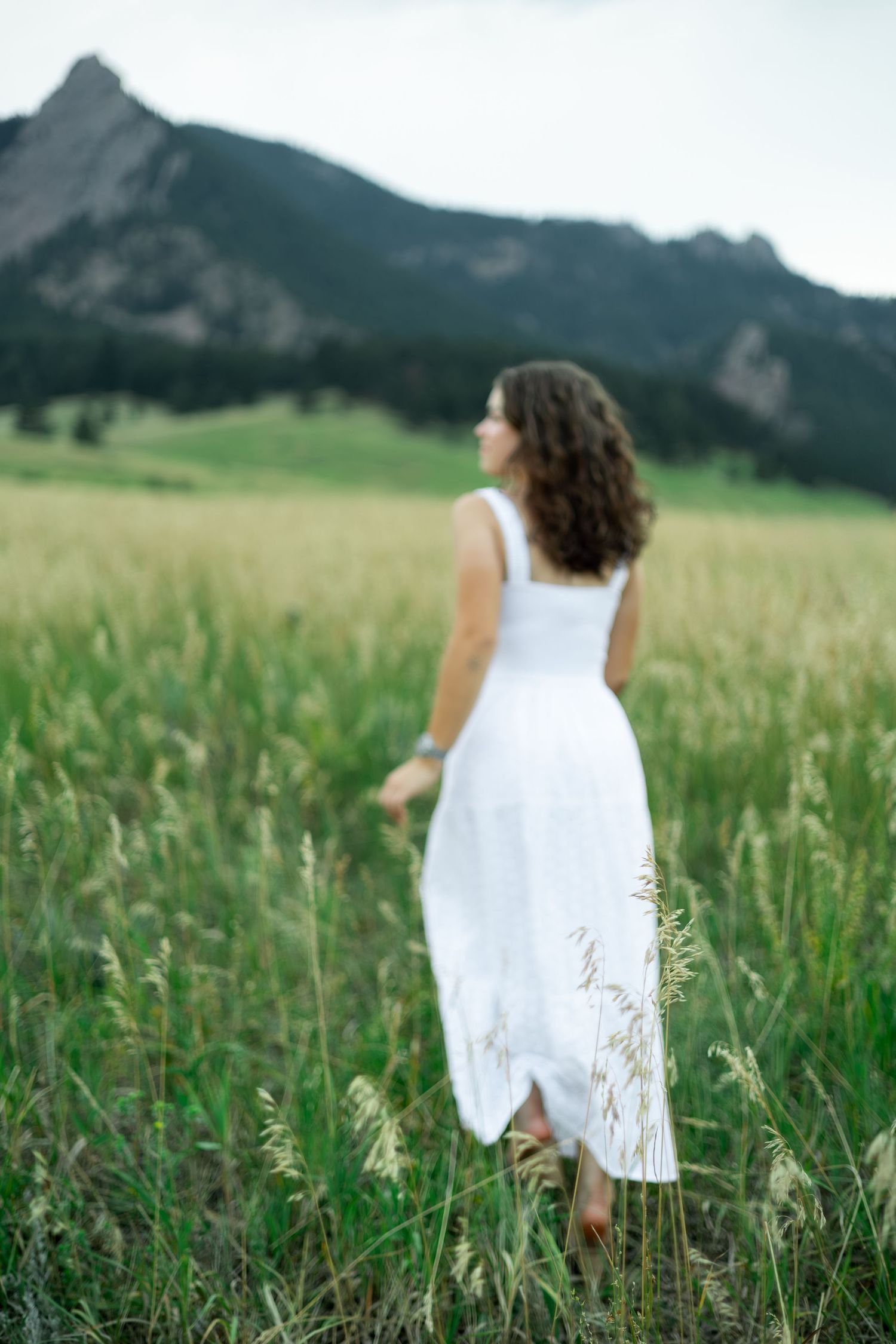 A flowing white sundress moves gracefully through a lush mountain meadow on a summer afternoon.
