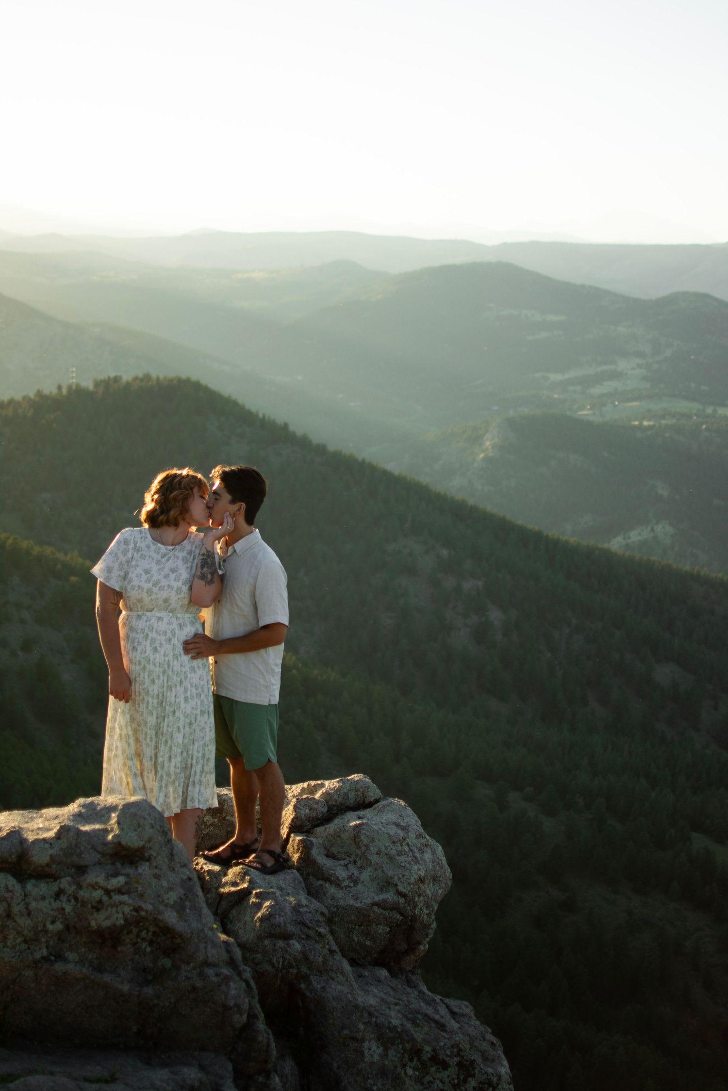 Romantic mountainside moment as couple stands on rocky overlook during golden hour.