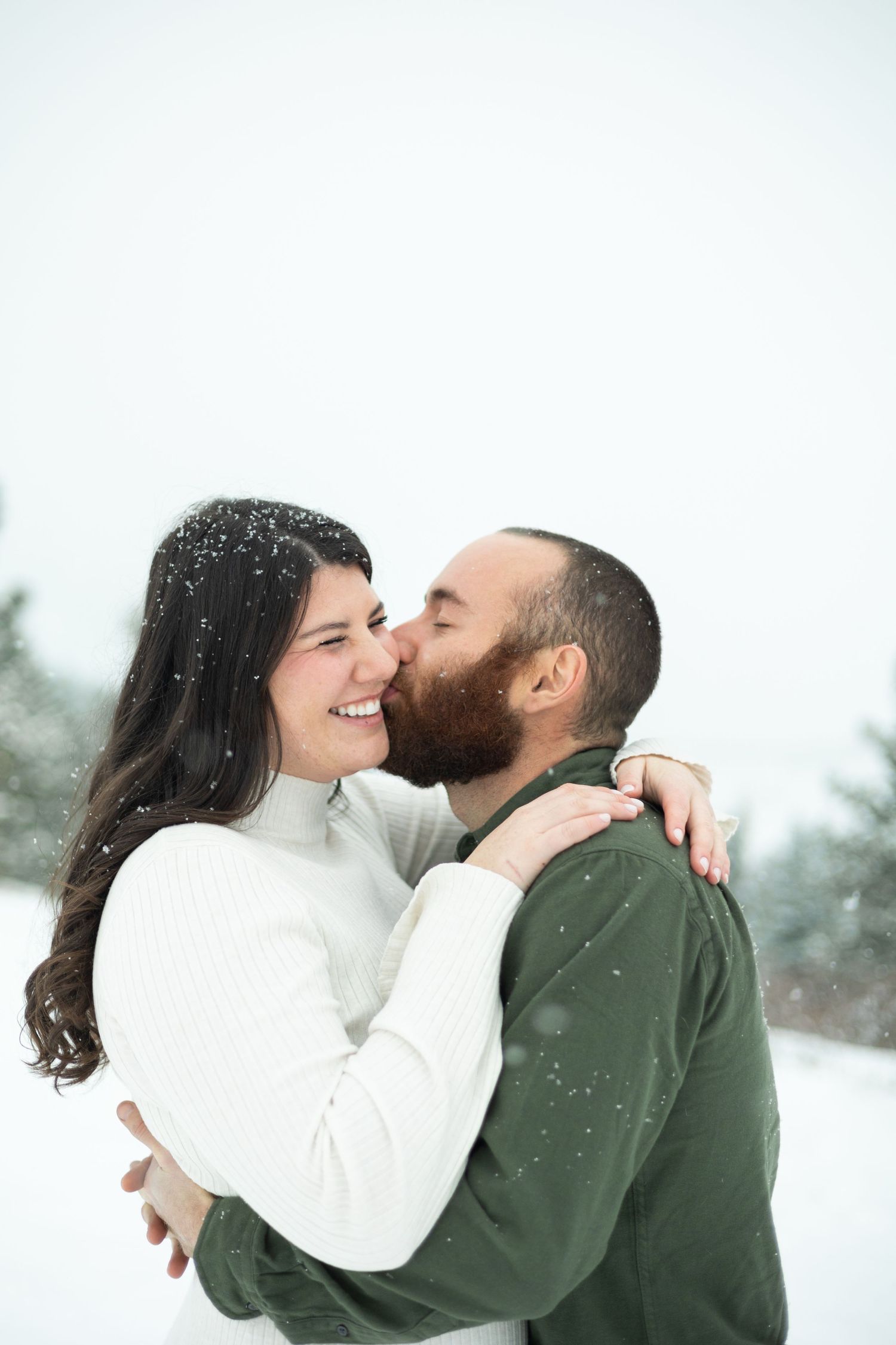 A romantic winter engagement photo showing a couple embracing in the falling snow.