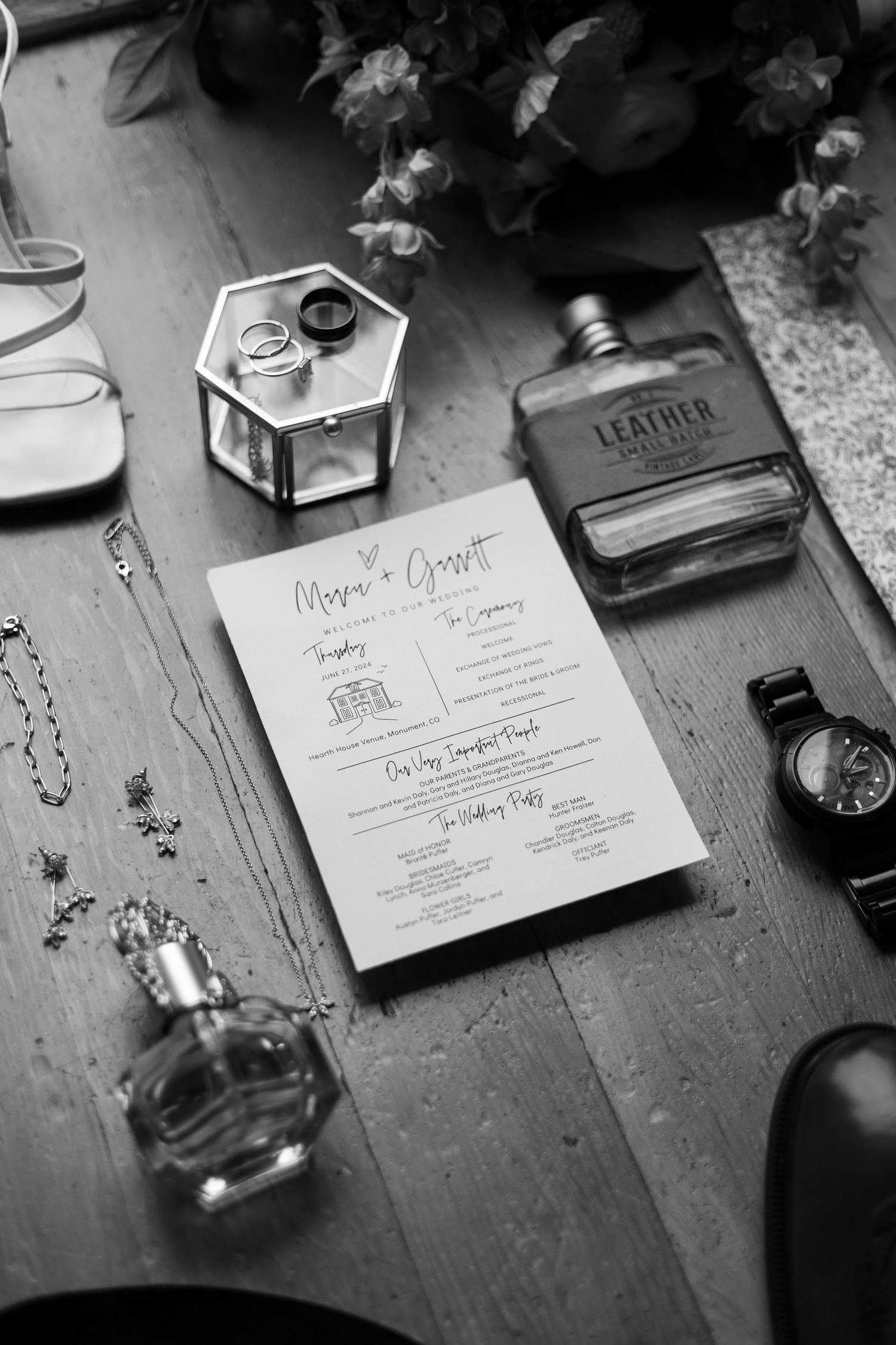 Wedding details flatlay with menu card, perfume bottles, and rings in monochrome style.