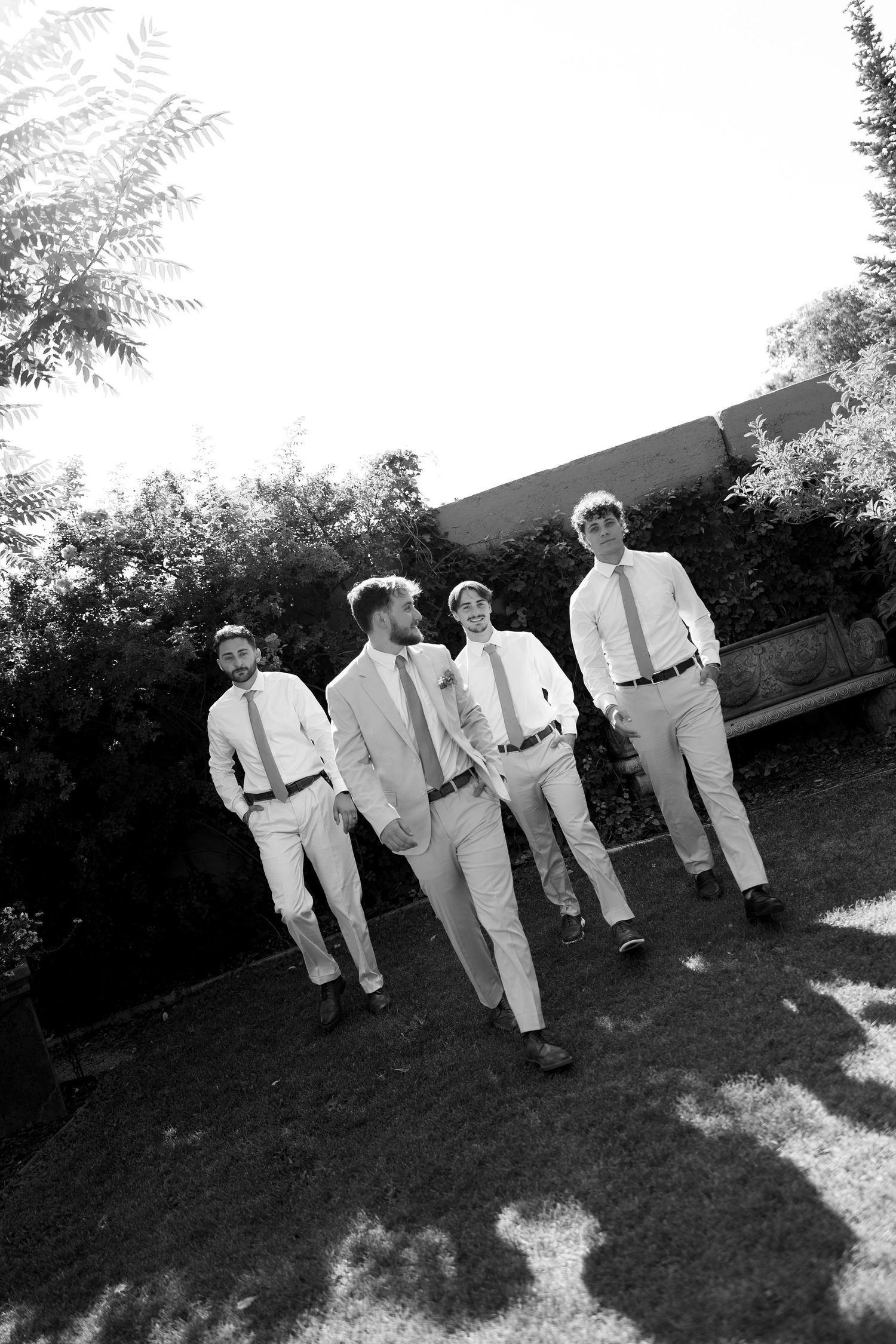 Four groomsmen in white shirts and ties walking outdoors in a black and white wedding photo.