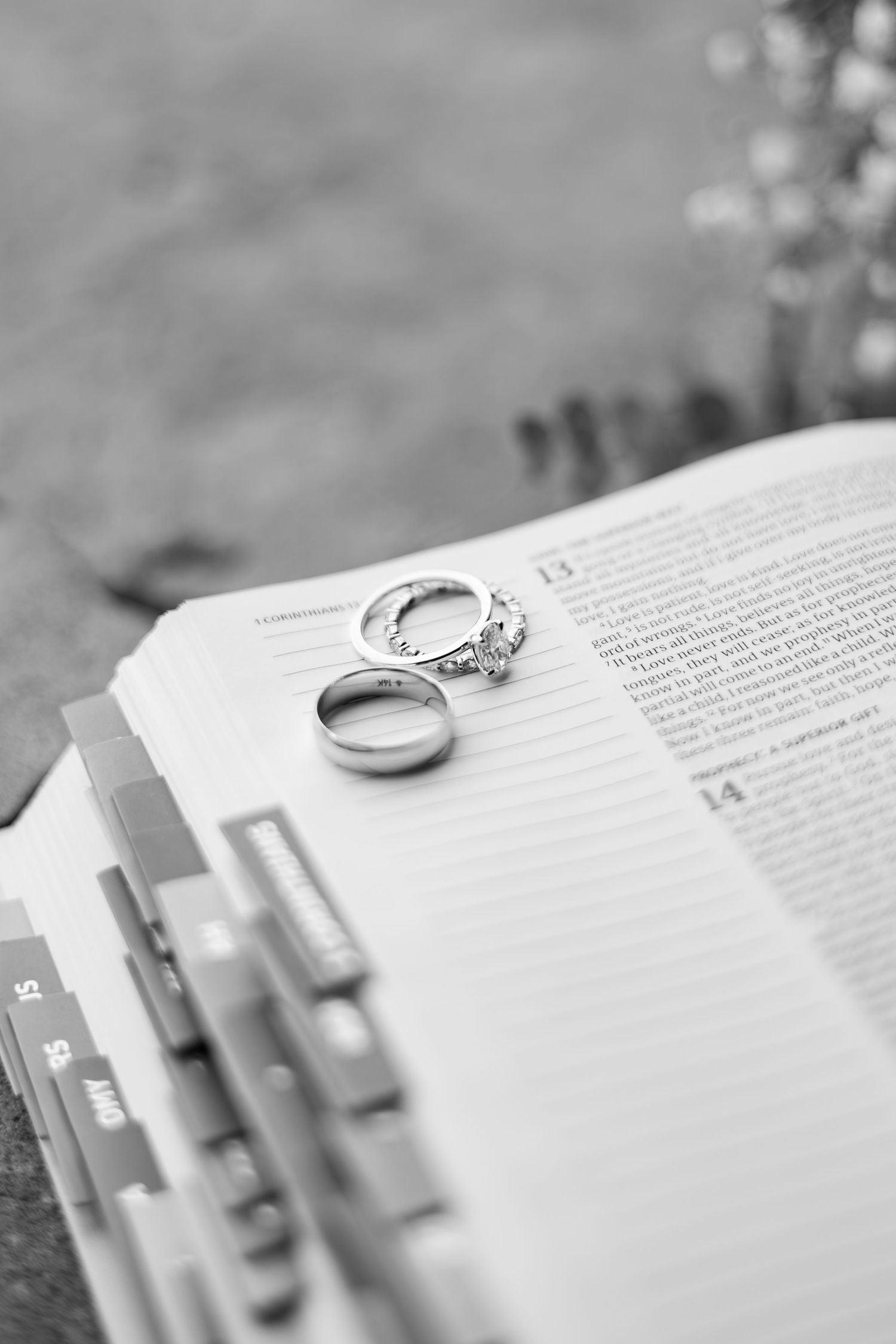 A silver wedding band rests atop an open book with tab dividers and page markers in soft black and white focus.