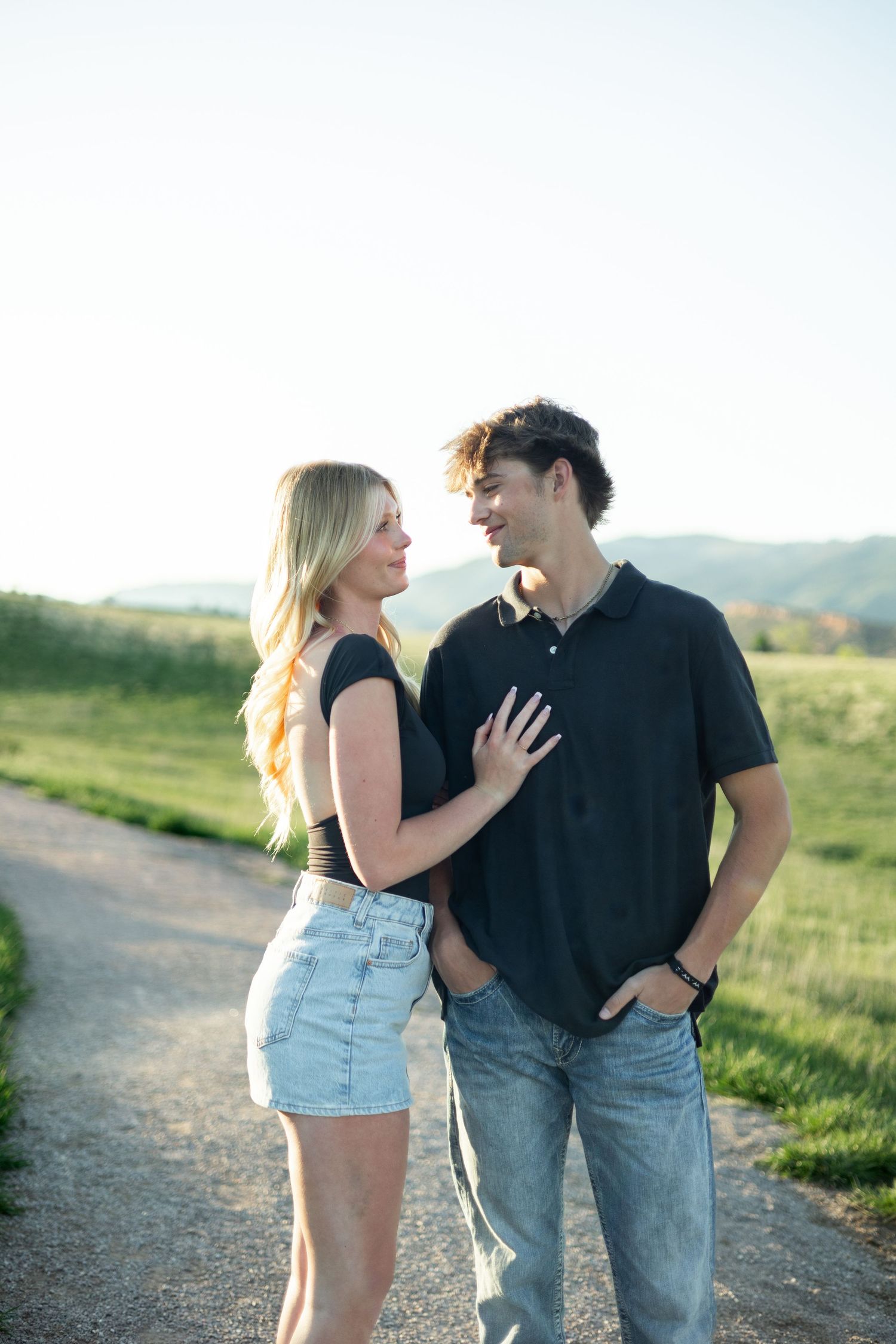 A couple sharing an intimate moment on a nature path with rolling hills in the background at sunset.