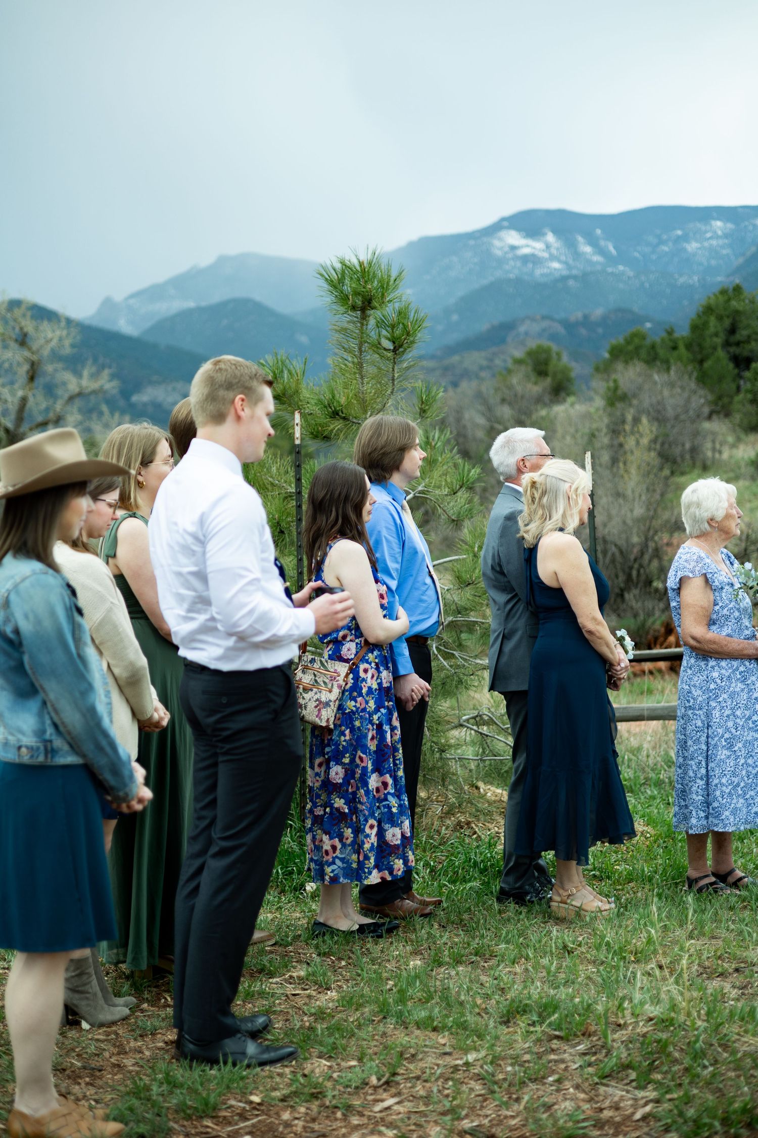 A group of people stand in a line against a backdrop of beautiful mountain scenery during an outdoor gathering.