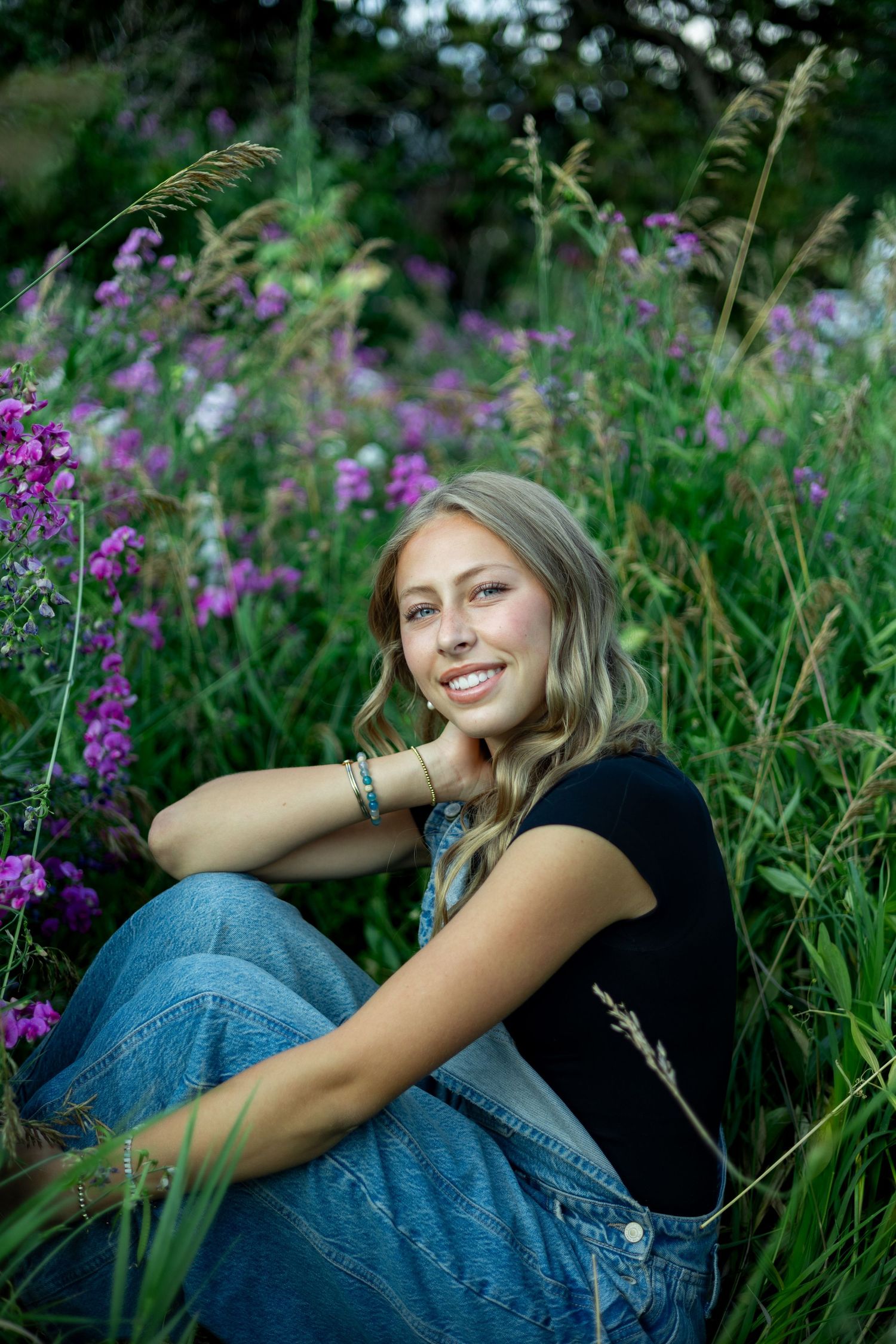 A dreamy outdoor portrait in a field of purple wildflowers with tall grass and natural lighting.