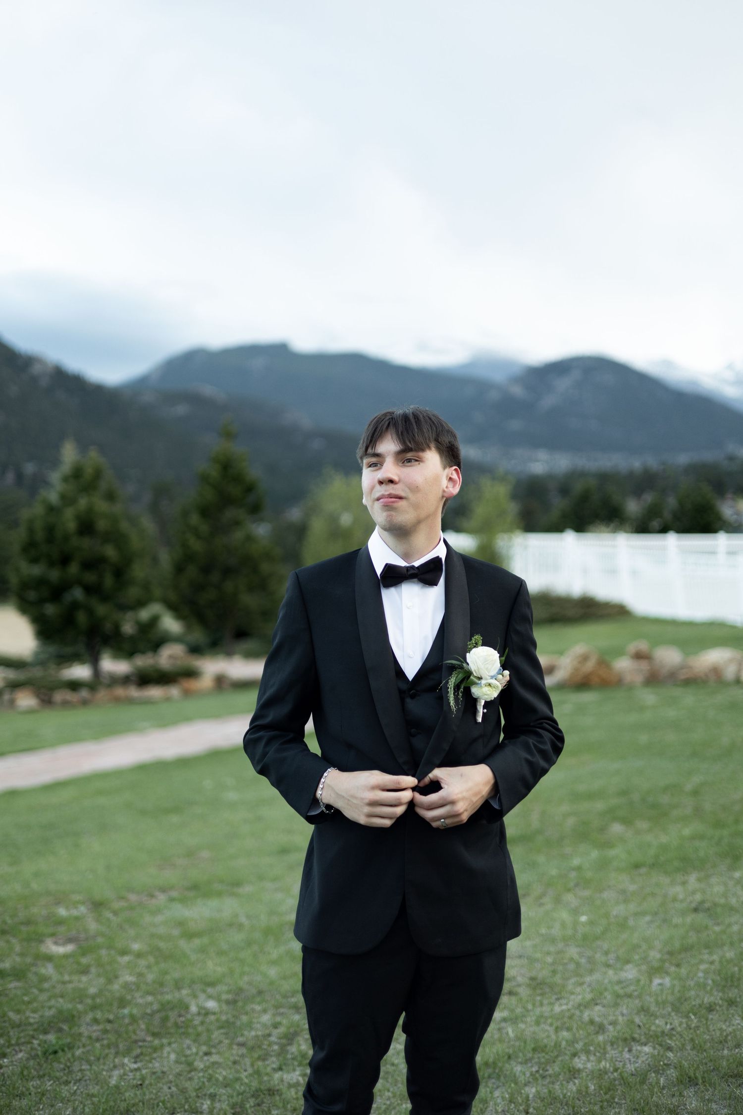 A scenic mountain landscape serves as backdrop for someone in formal attire on grassy terrain.