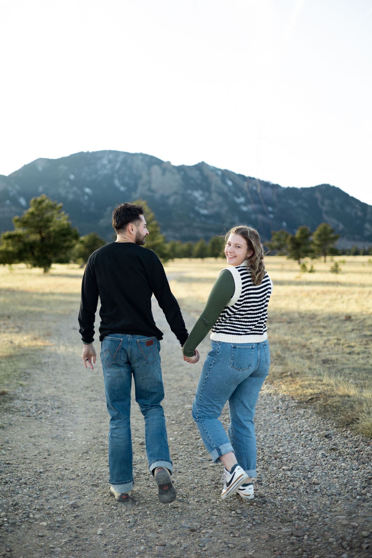 A couple walking hand in hand on a trail with scenic mountain views behind them.