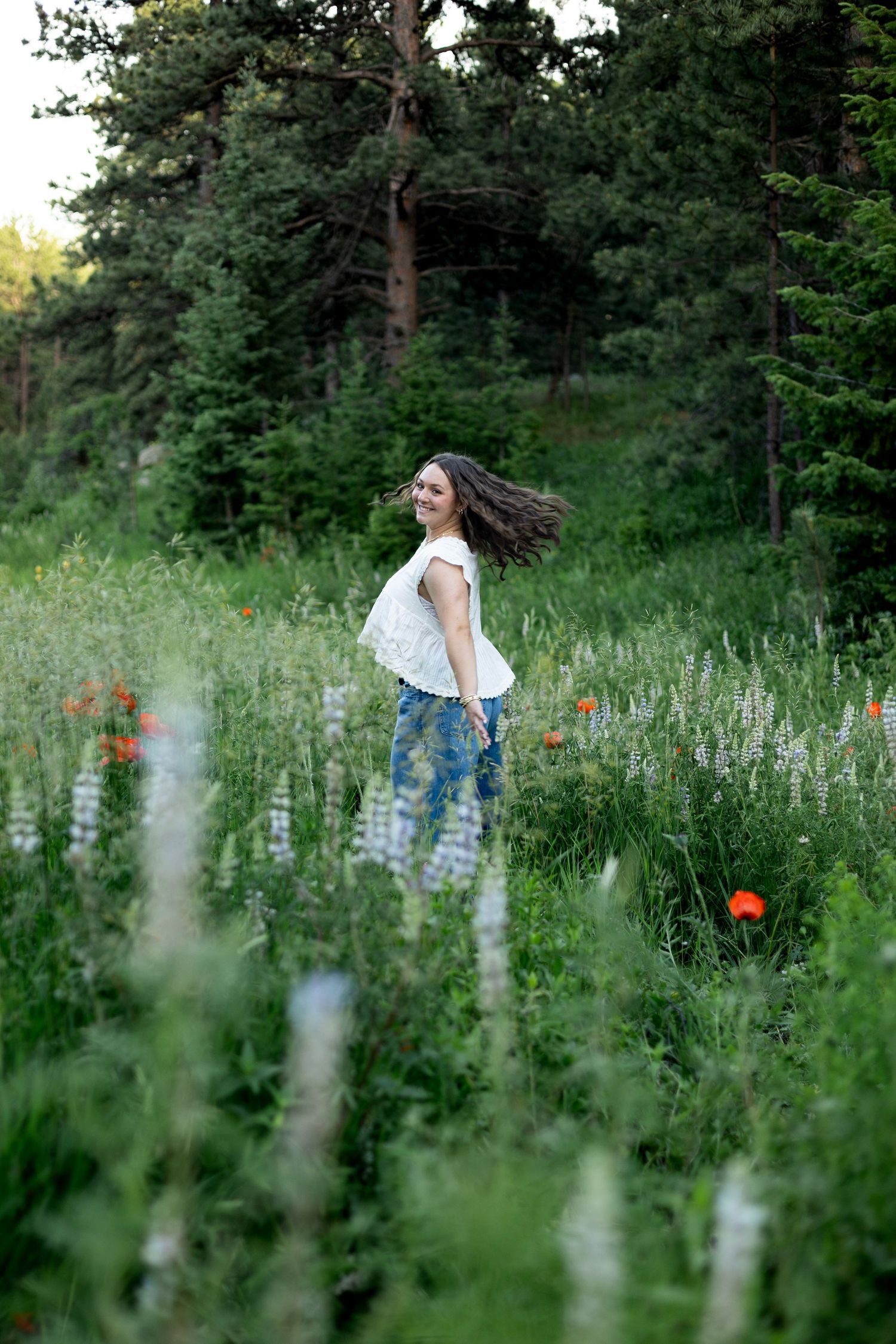 A person stands amid a lush meadow of wildflowers and tall grass in a tranquil woodland setting during golden hour.