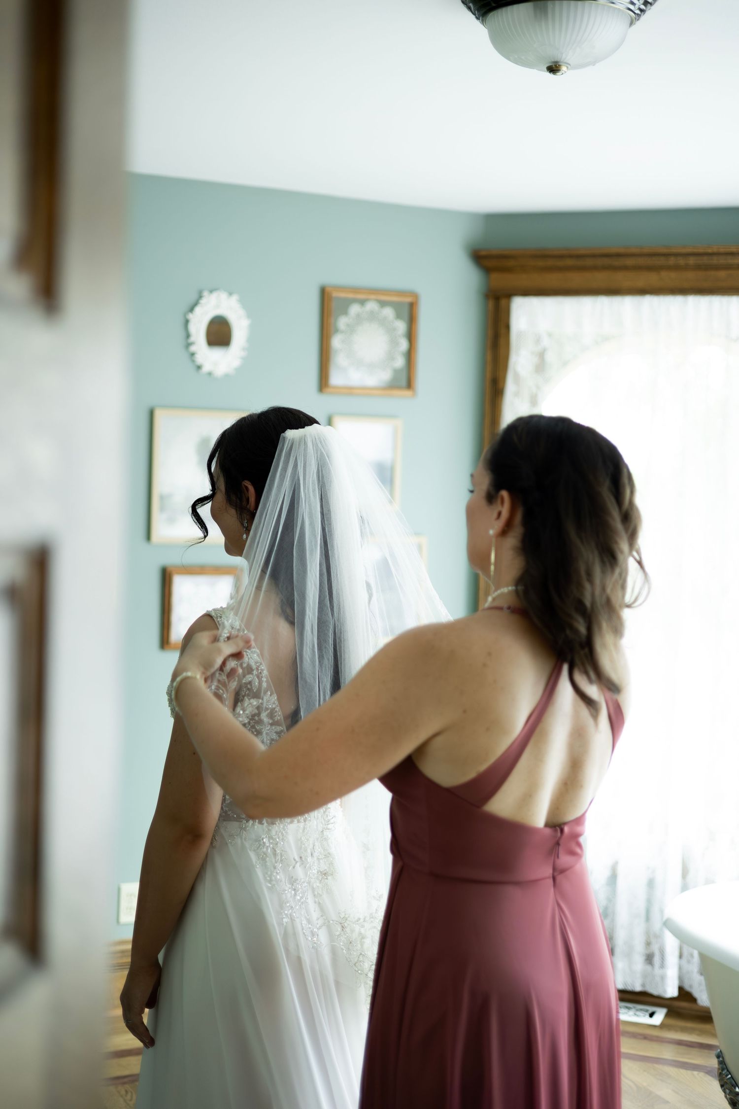A white wedding dress hangs elegantly as bridesmaids in burgundy dresses prepare for the special day.