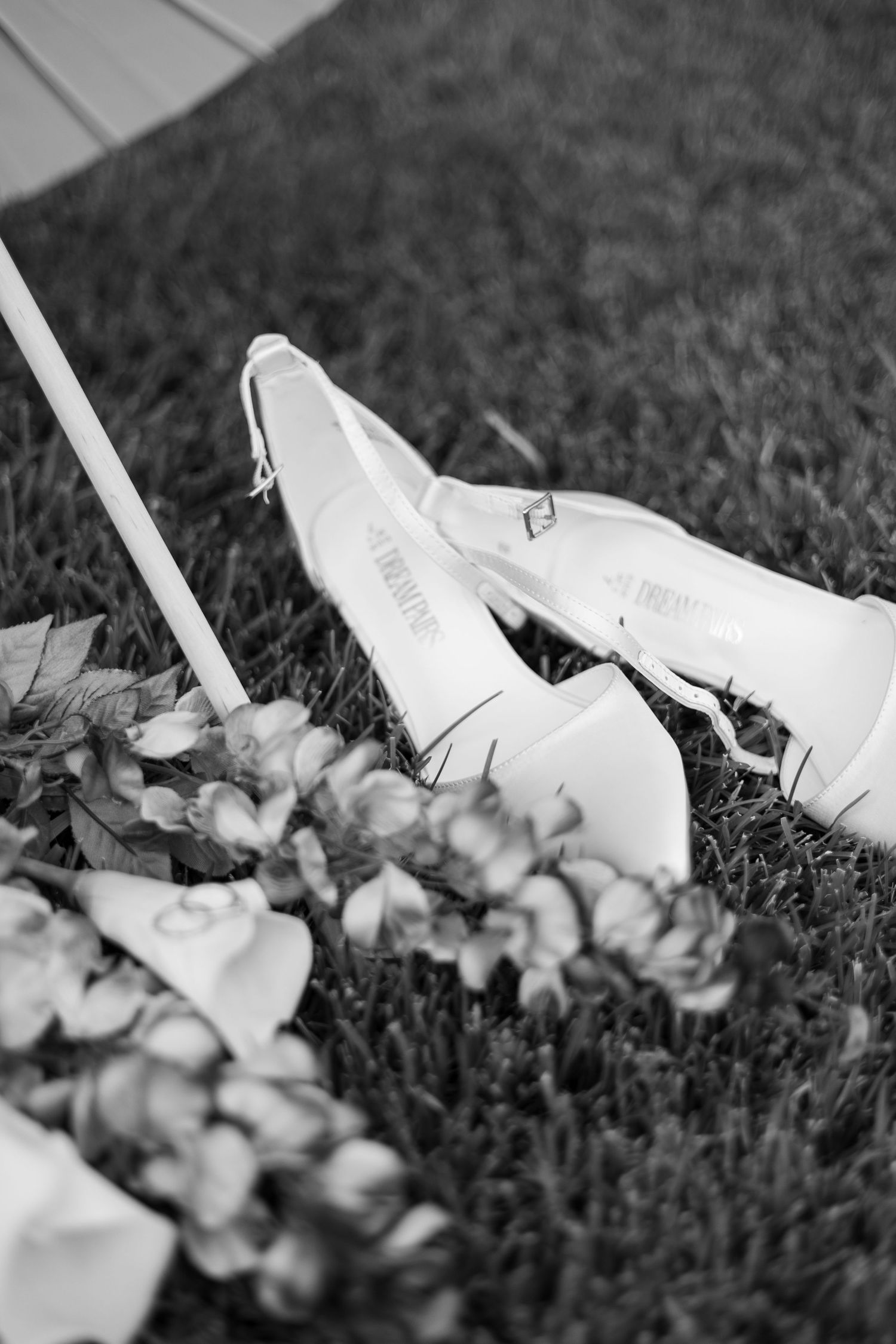 White ballet pointe shoes laying in grass with delicate flowers creating an artistic black and white composition.
