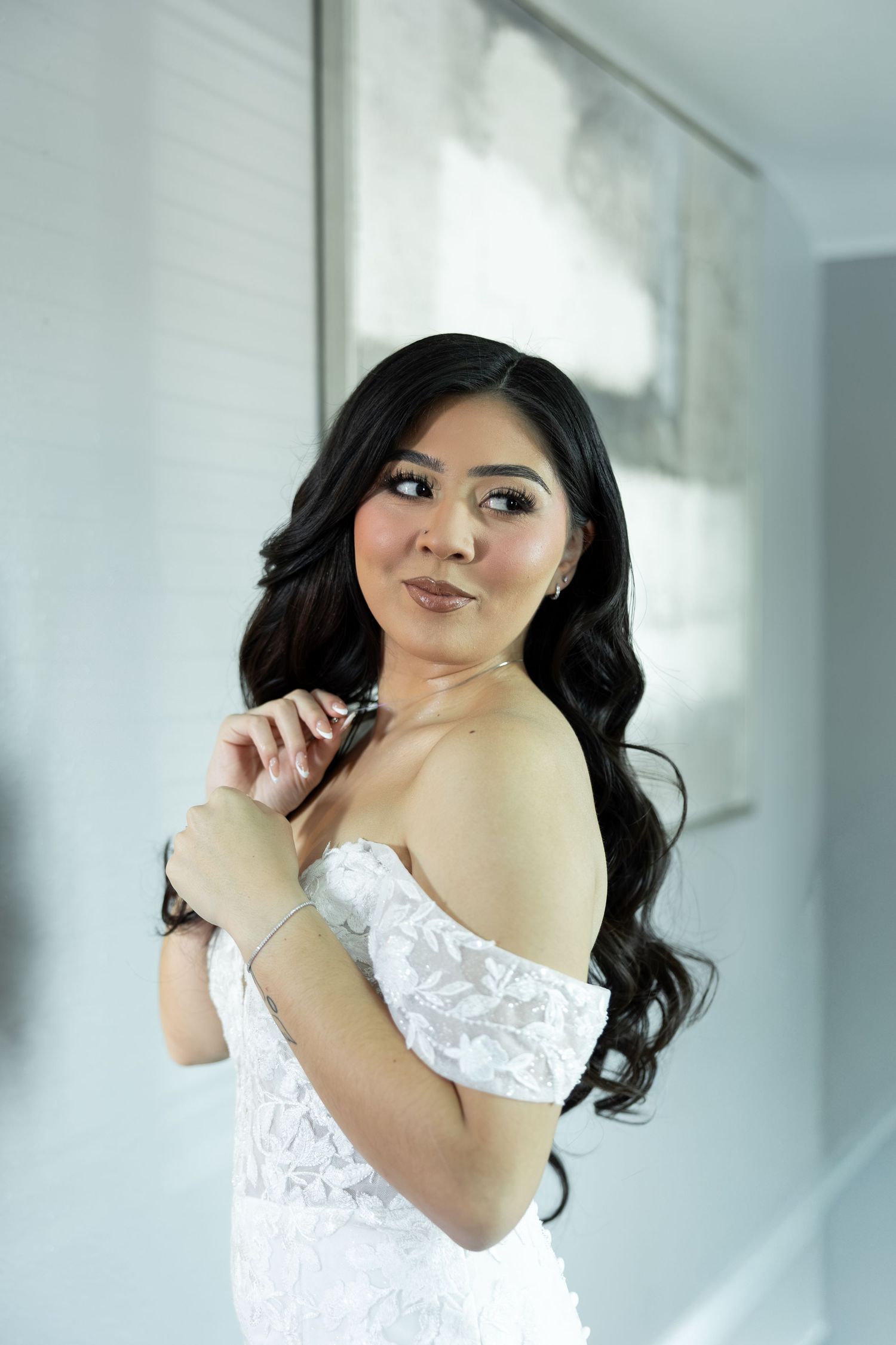 A woman in a white lace dress poses against a bright window background.