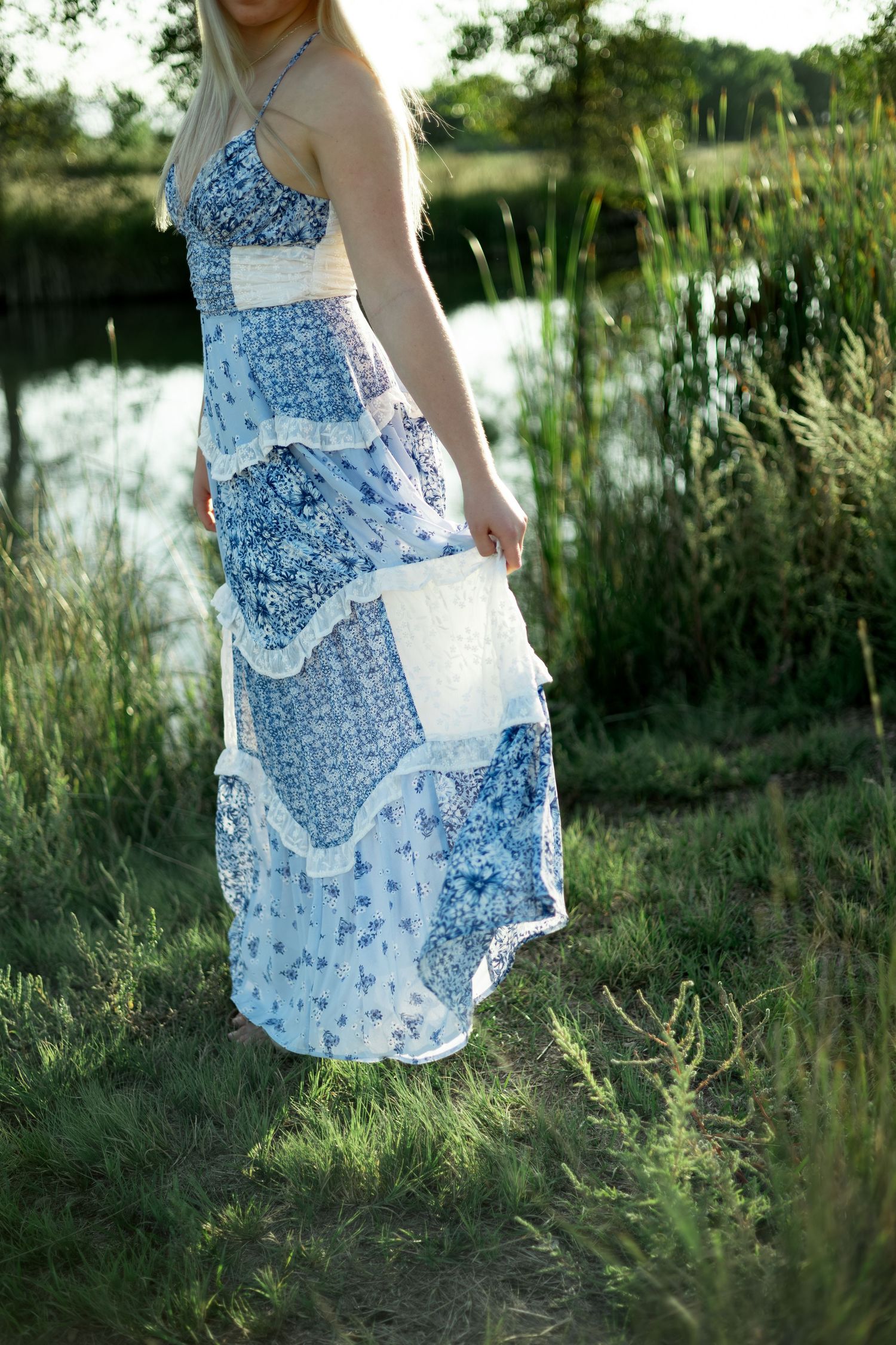 A flowing blue and white floral dress sways in a natural setting by a pond with wild grasses.