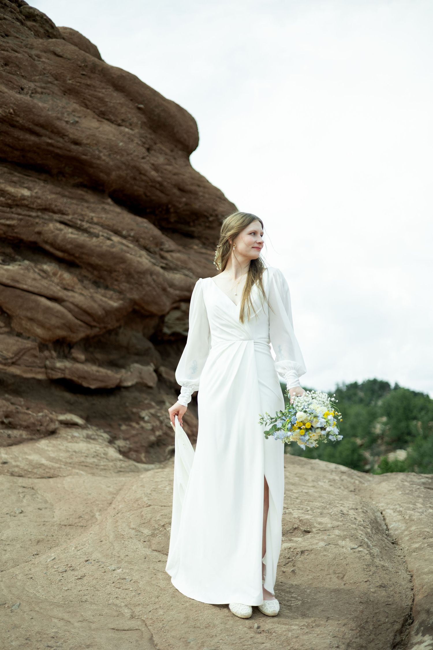 A figure in a flowing white dress poses against dramatic red rock formations in an artistic outdoor photoshoot.