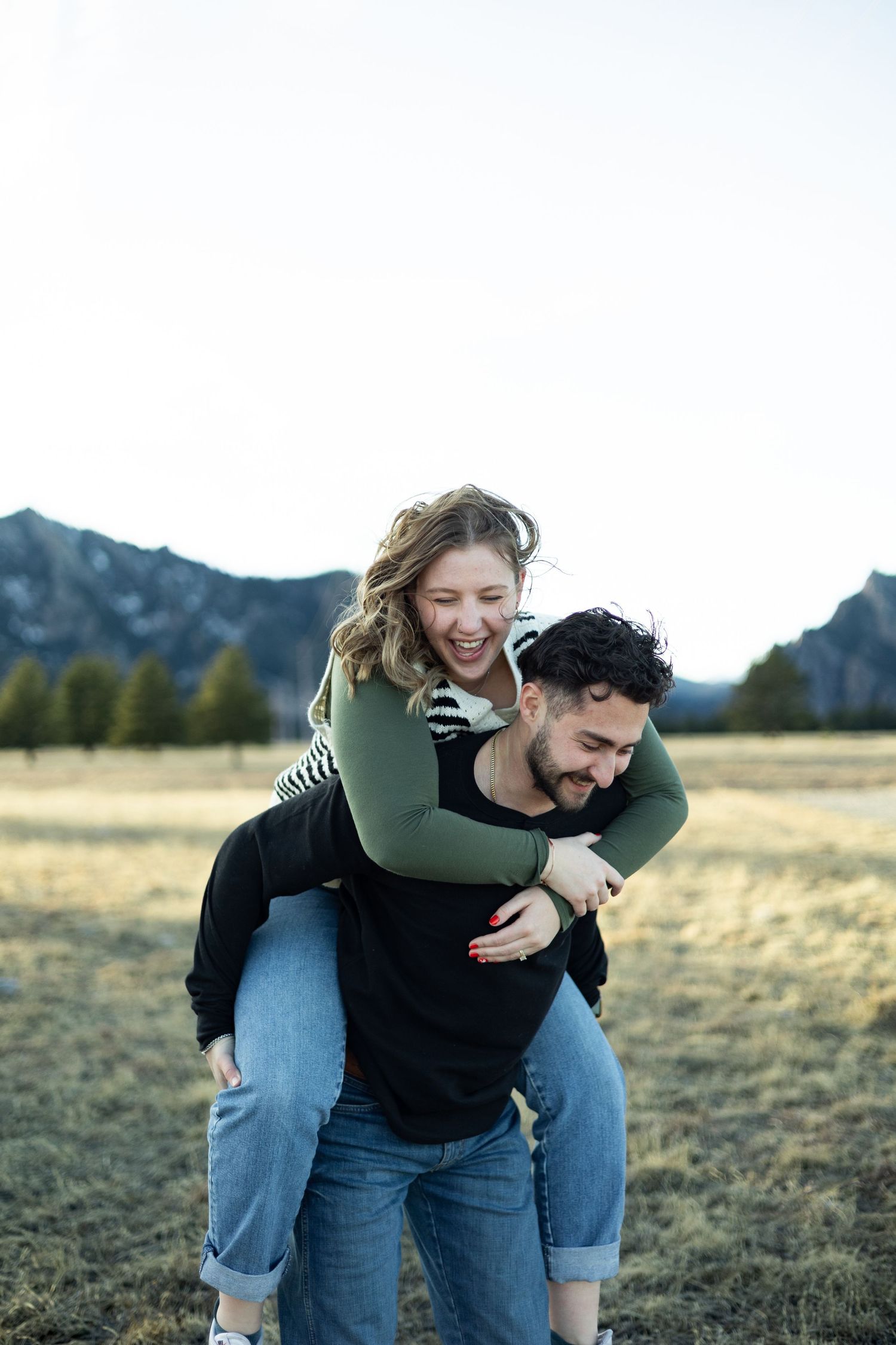 A playful piggyback ride moment captured against a mountain backdrop in a grassy field.