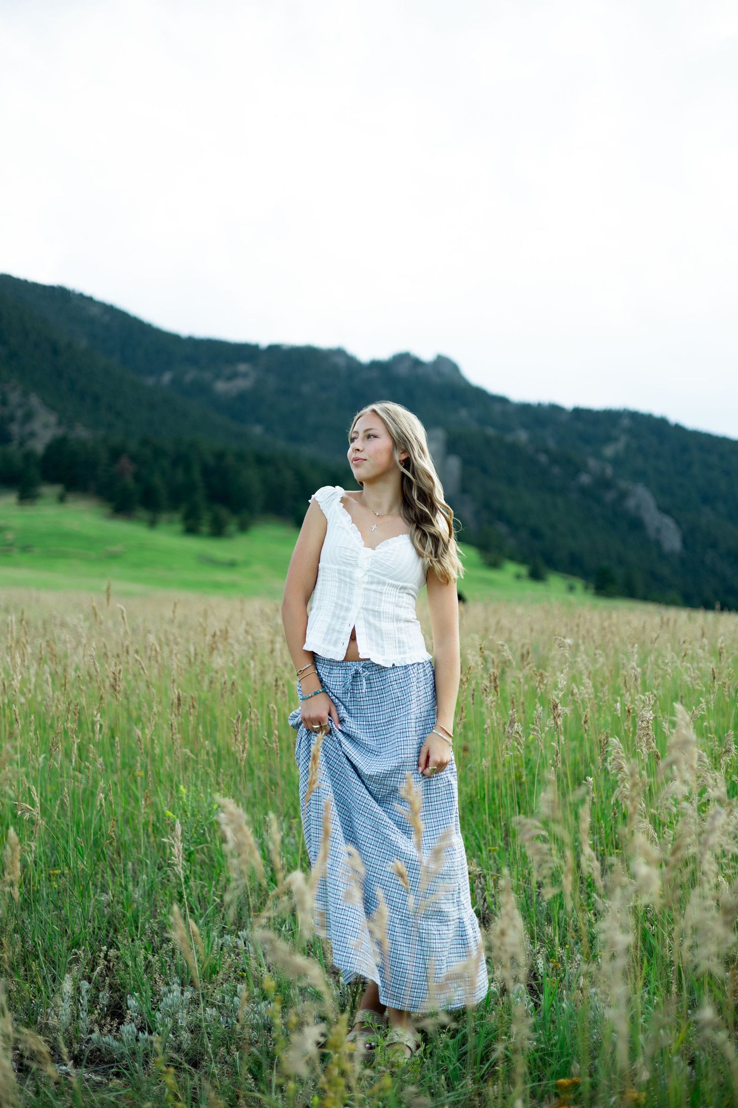 A serene meadow scene with long grass and mountains showcases summer fashion with a flowing long skirt and white top.