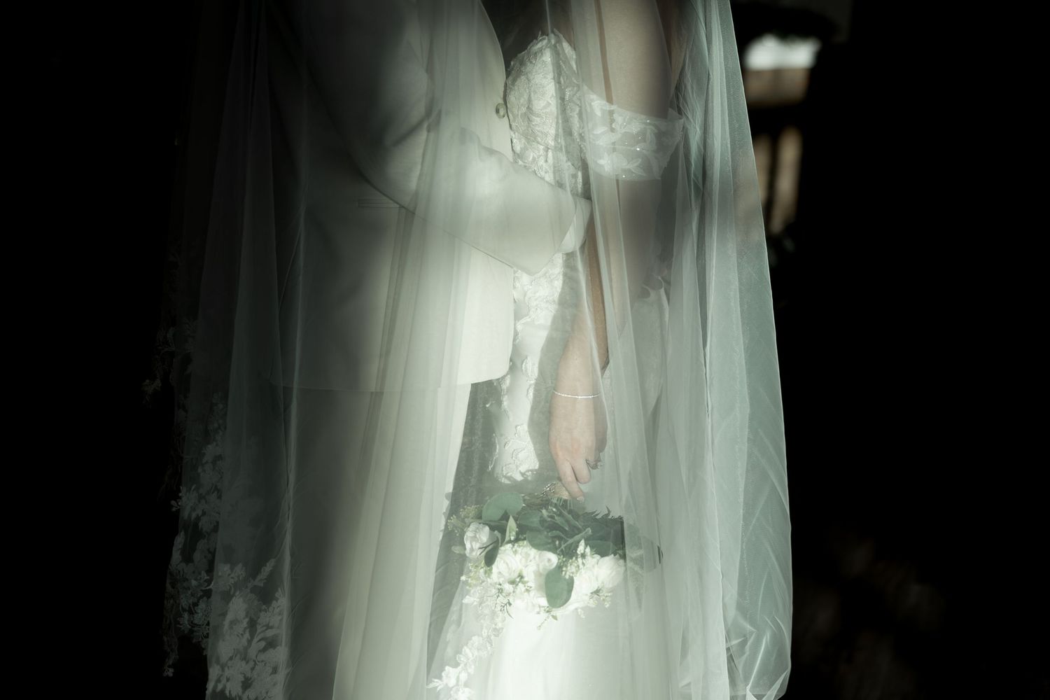 A flowing white wedding veil with delicate lace details billows gracefully in the light.